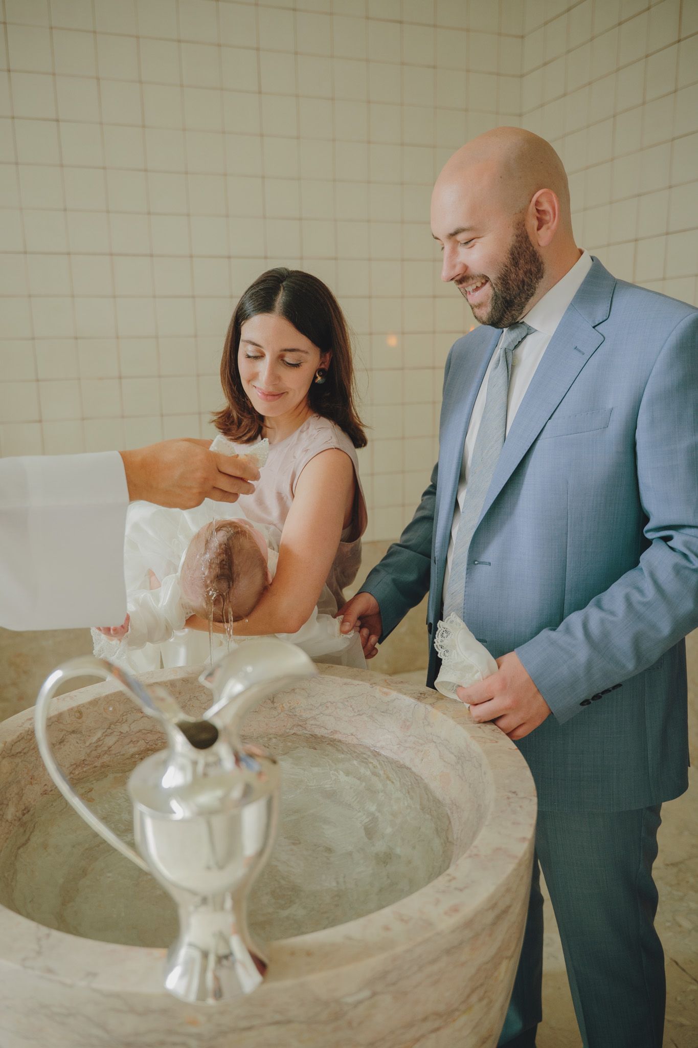 A baptismal ceremony takes place around a stone font in a modern church setting.