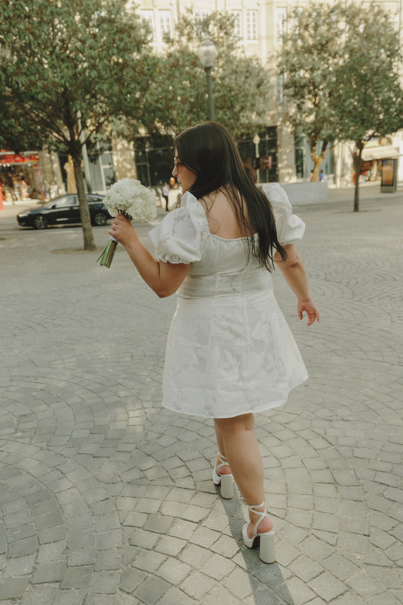 A playful figure in a white dress twirling on a cobblestone plaza.