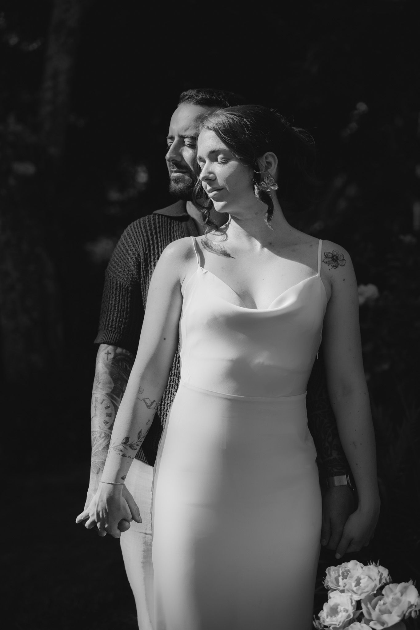 Artistic black and white portrait of newlyweds in elegant attire against dark background.