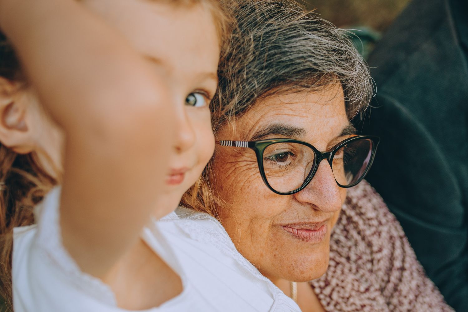 A person wearing glasses and a pink floral shirt shares a warm moment with a child in a light-colored dress.