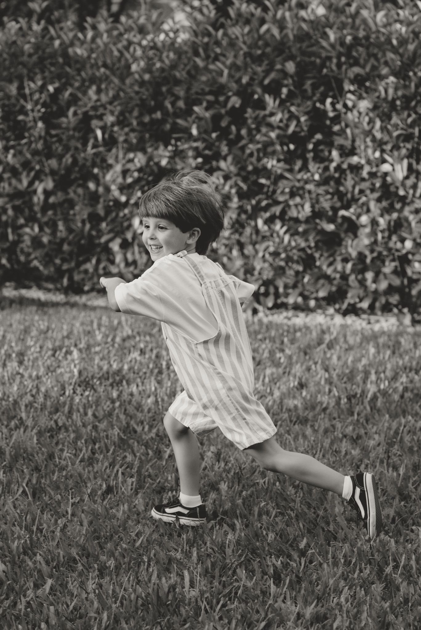 A person in white clothing leaps gracefully across a grassy field in black and white.
