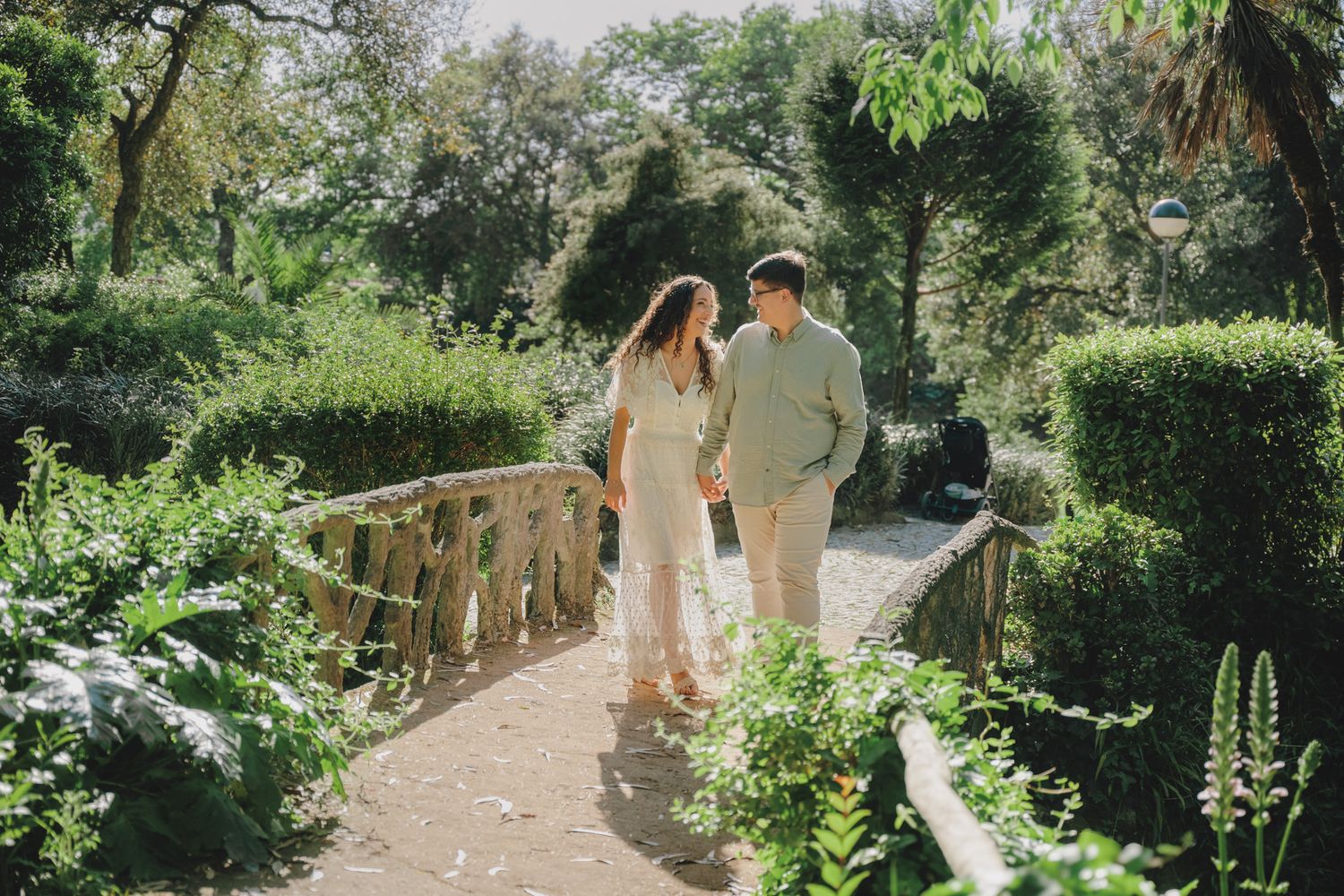 Couple strolling through a sunlit garden pathway with vibrant greenery.
