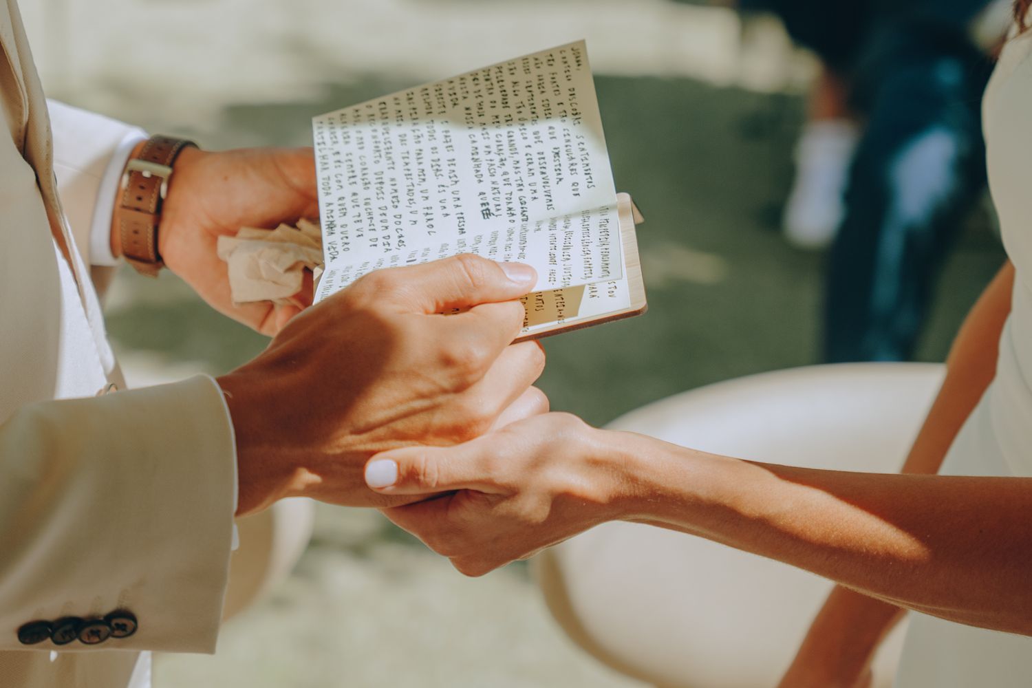 Hands exchange handwritten notes during what appears to be a wedding ceremony with sunlight in the background.