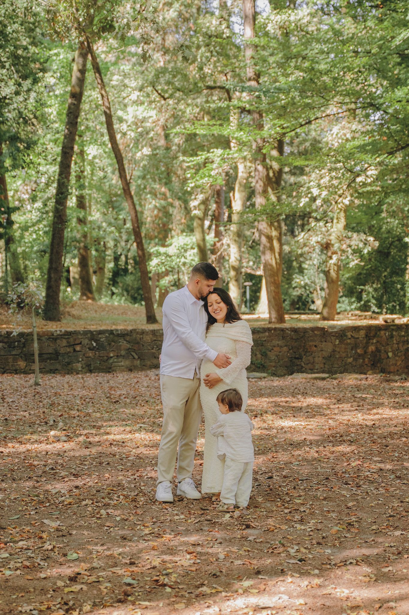 A family shares an intimate moment together on a forest path covered in fallen leaves.