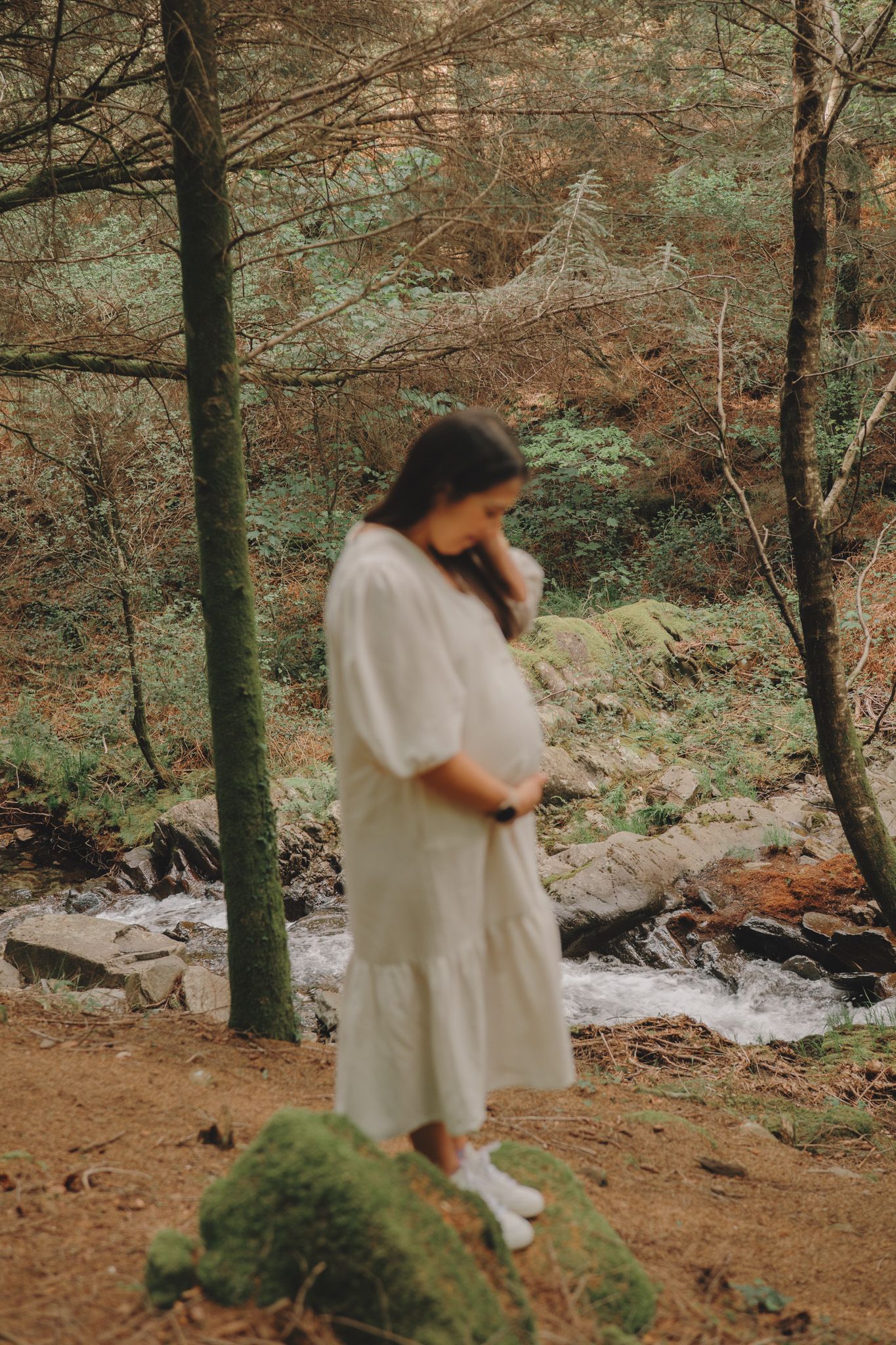 Someone in a light-colored dress walks through a peaceful woodland setting.