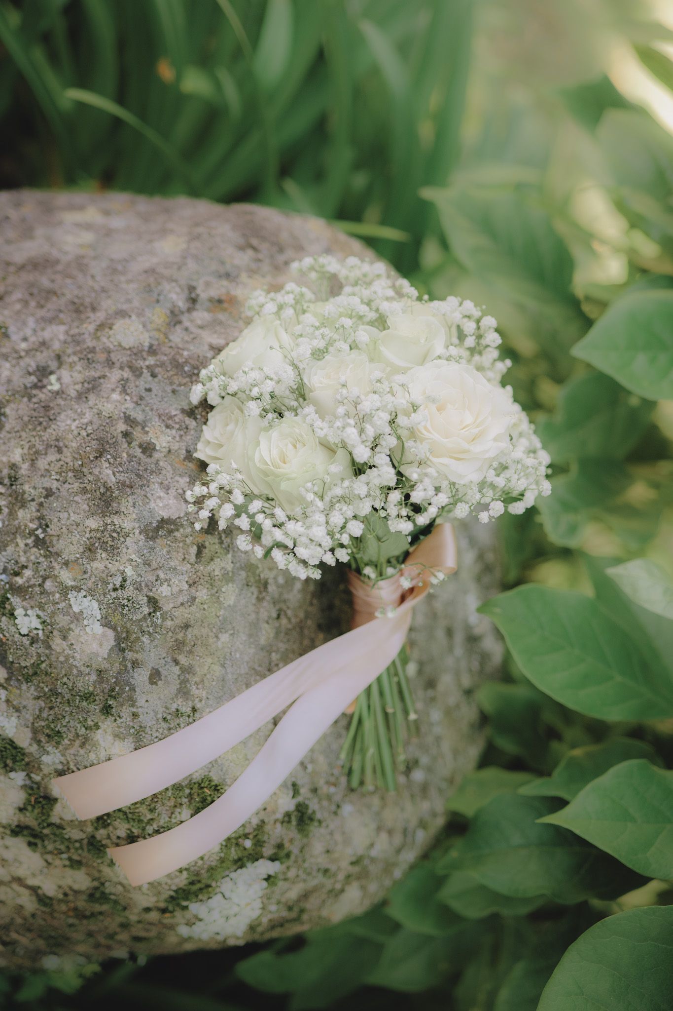 White wedding bouquet with delicate flowers and ribbon resting on a stone surface.