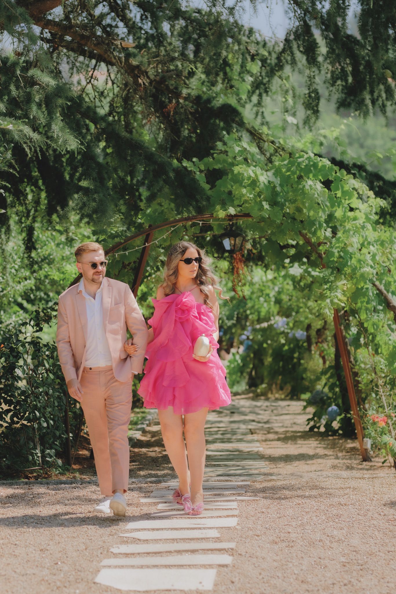 Couple walking along garden path wearing matching pink and peach outfits.
