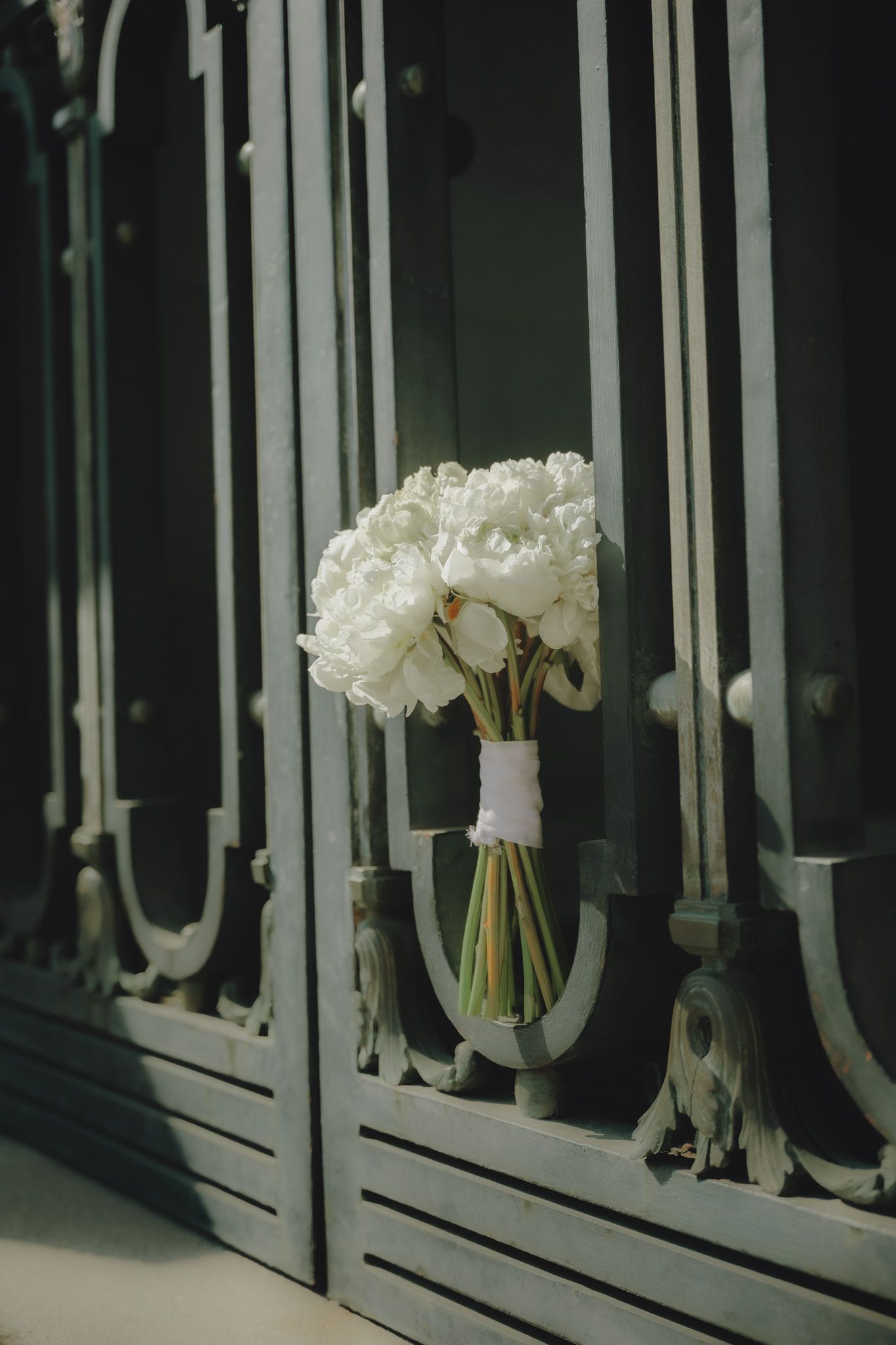 White peonies in glass vases arranged against an ornate dark window frame with decorative metalwork details.