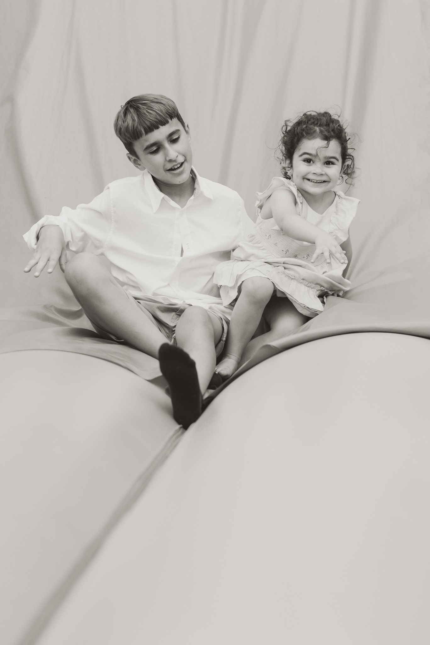 Black and white photo of playful children lounging on light colored furniture.