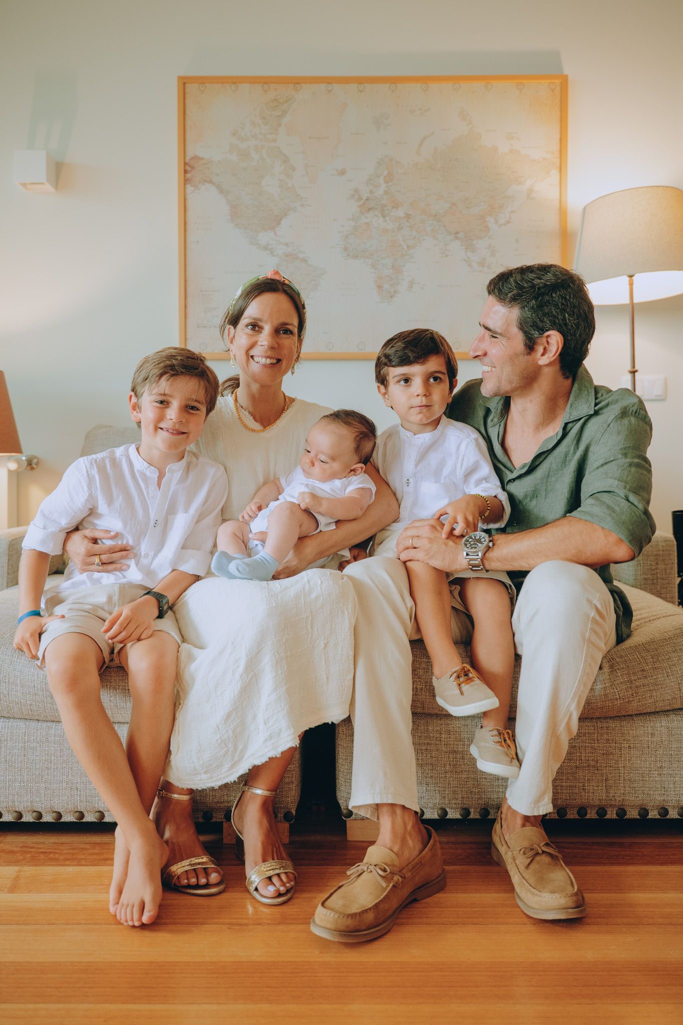 Family sitting together on floor against wall with world map, wearing coordinated white outfits.