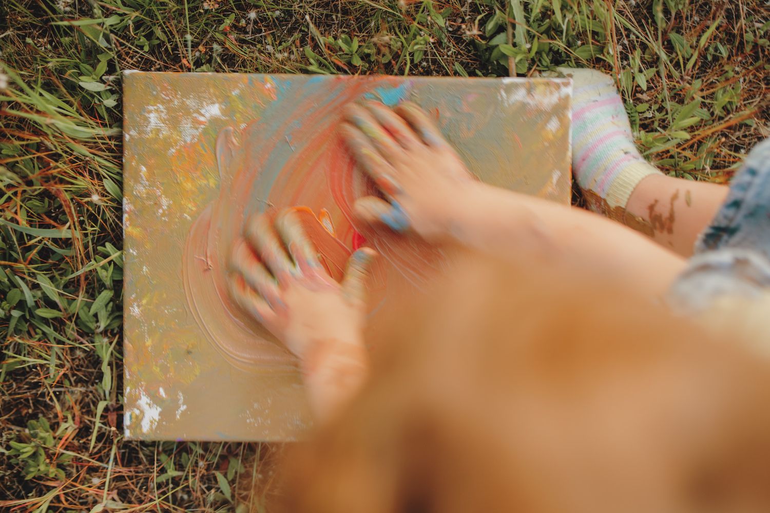 Hands smearing paint on a canvas in an outdoor art session.