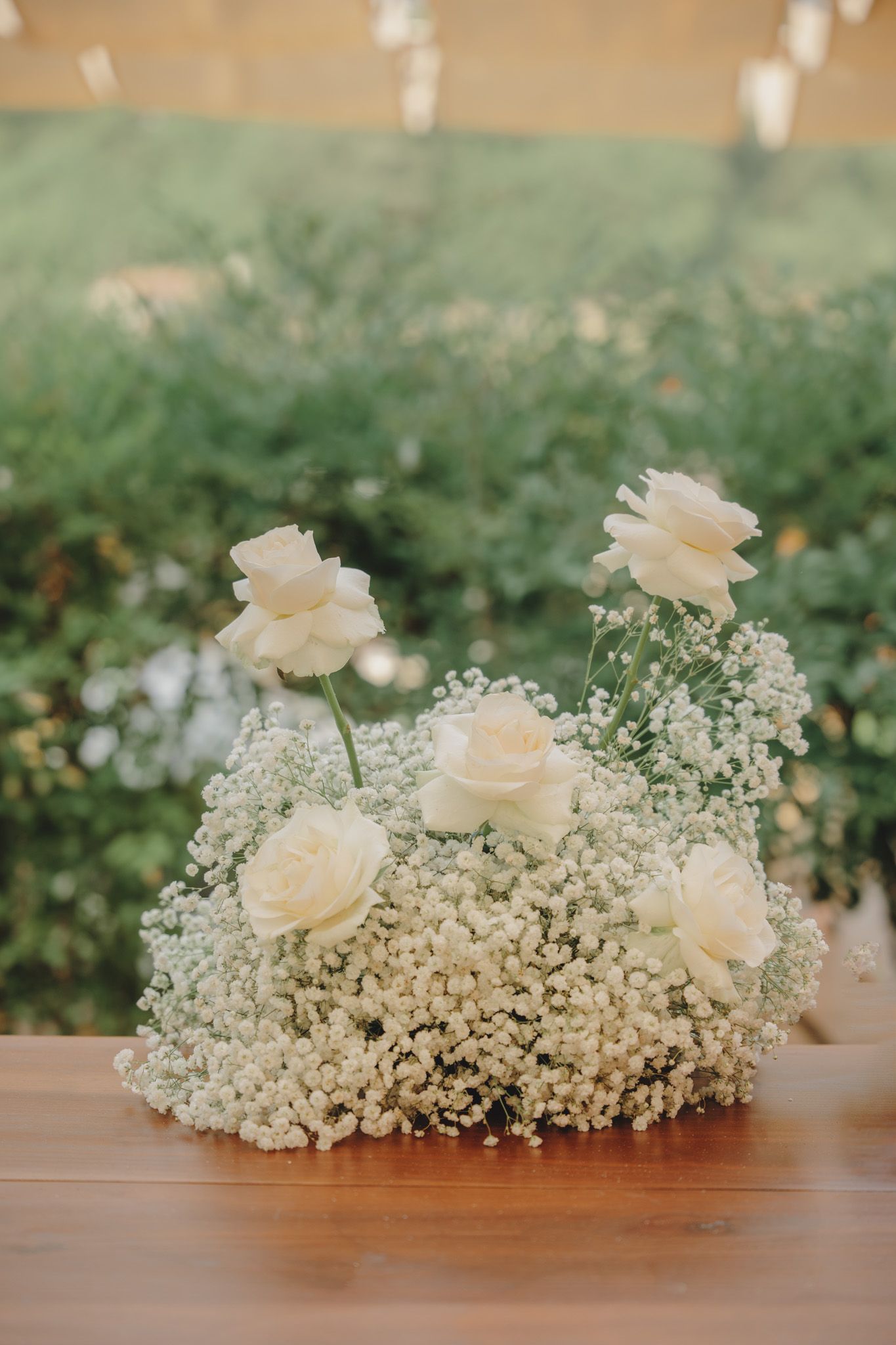 White roses and baby's breath floral arrangement on wooden surface.