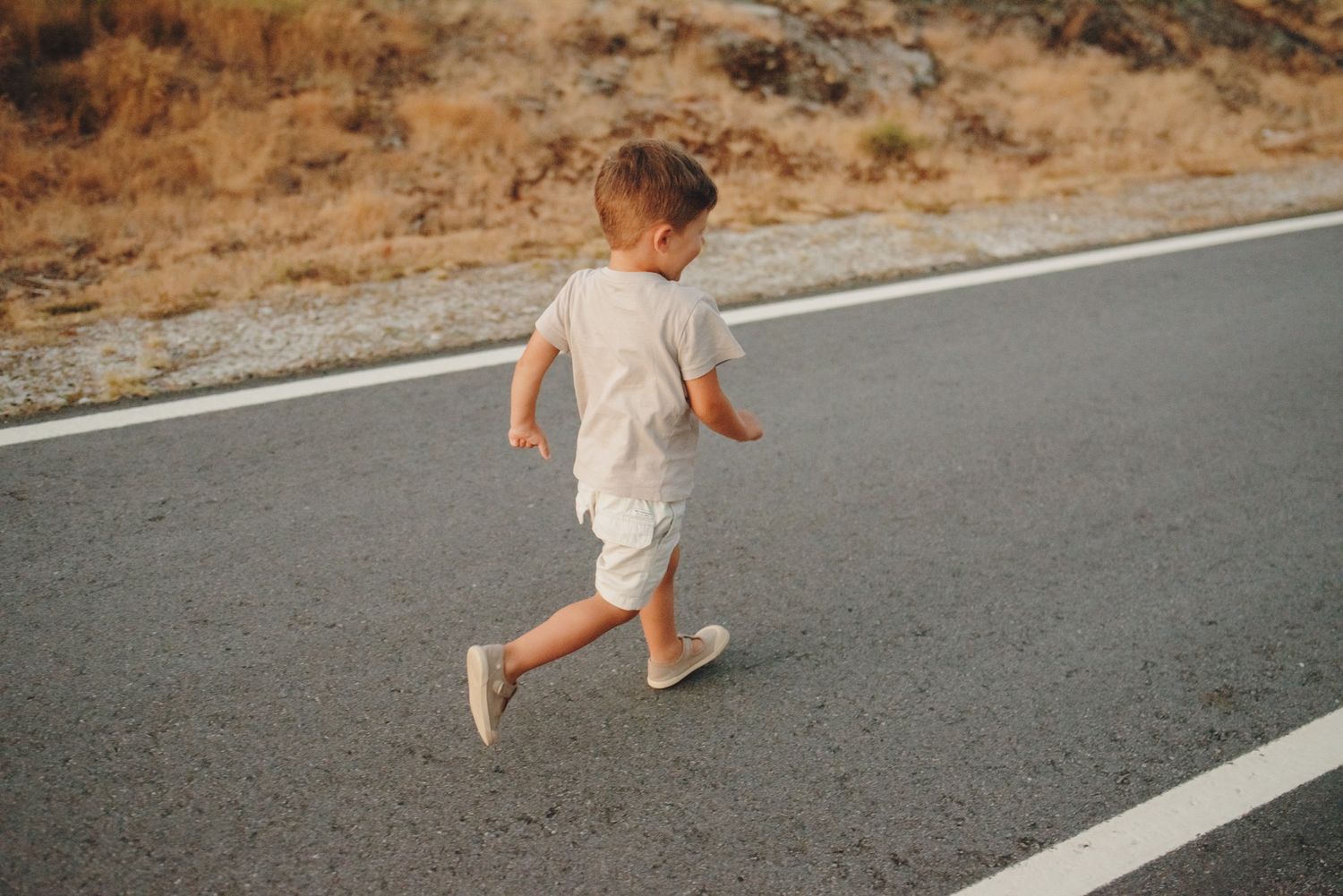 Small child running on an empty road through a desert landscape.