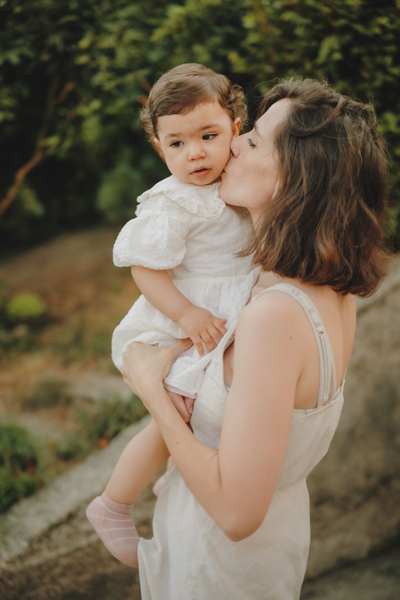 Tender moment captured in outdoor portrait with white summer dresses and natural lighting.