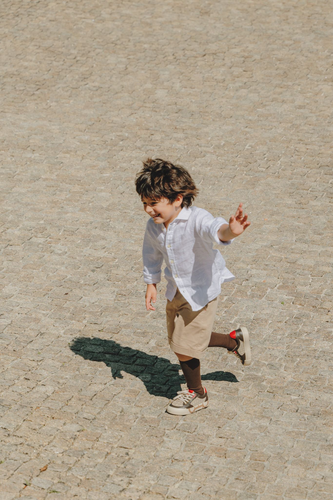 Sequence of a child running and leaping across a stone courtyard in casual attire.