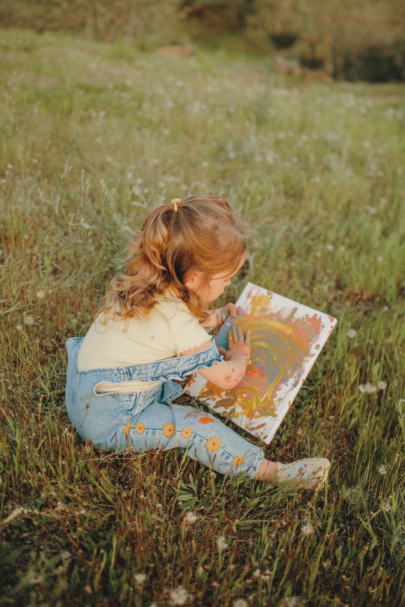 A small child relaxes in the grass while reading an open book outdoors.