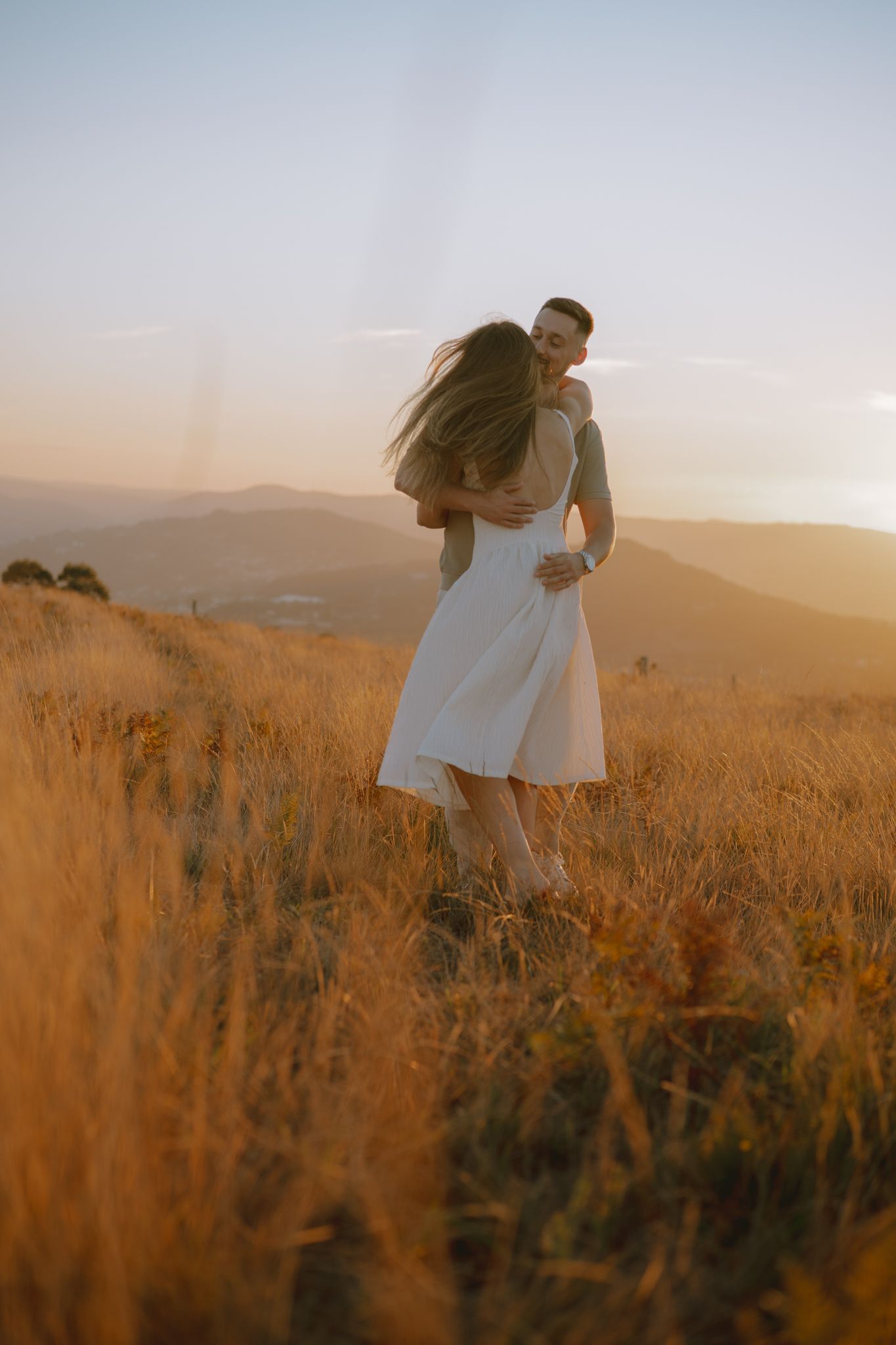 Two people share romantic moments in a golden field during sunset.