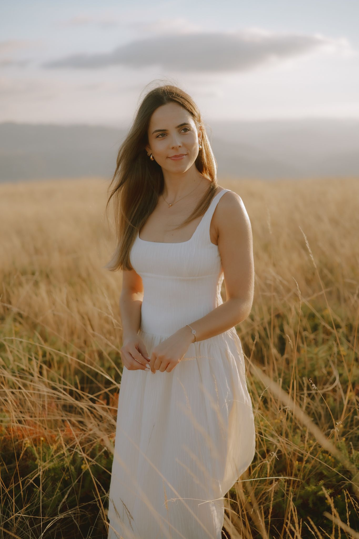 Woman in white dress poses gracefully in a sunlit field of tall grass.