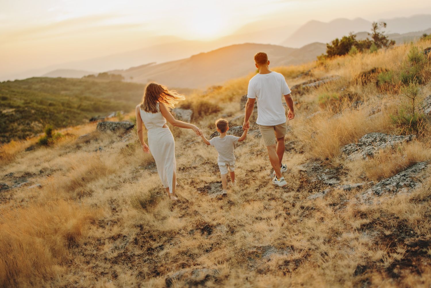 A couple walks along a scenic mountain trail at golden hour while holding hands and enjoying the sunset views.