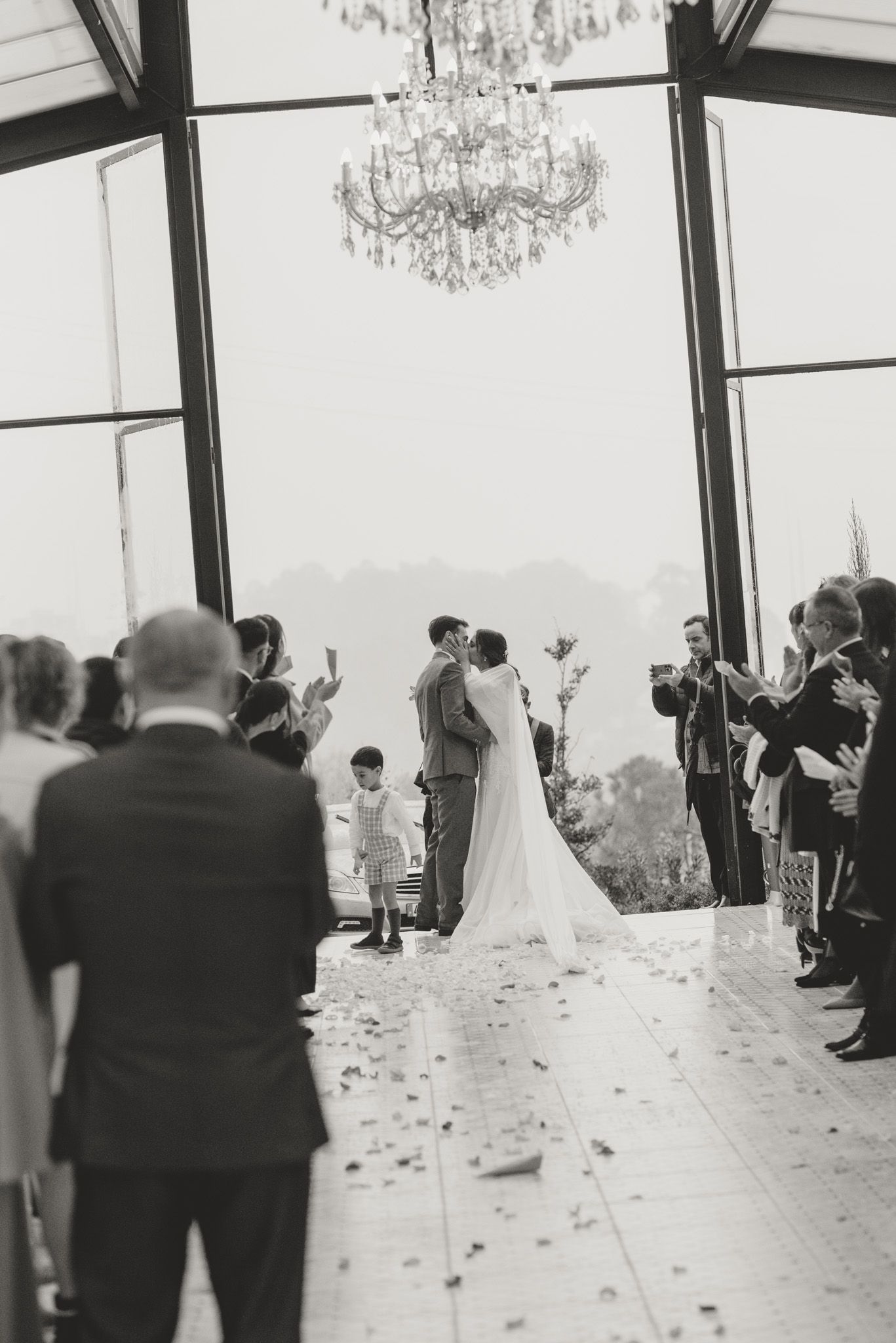 Wedding ceremony guests gather under elegant crystal chandeliers in an indoor venue.