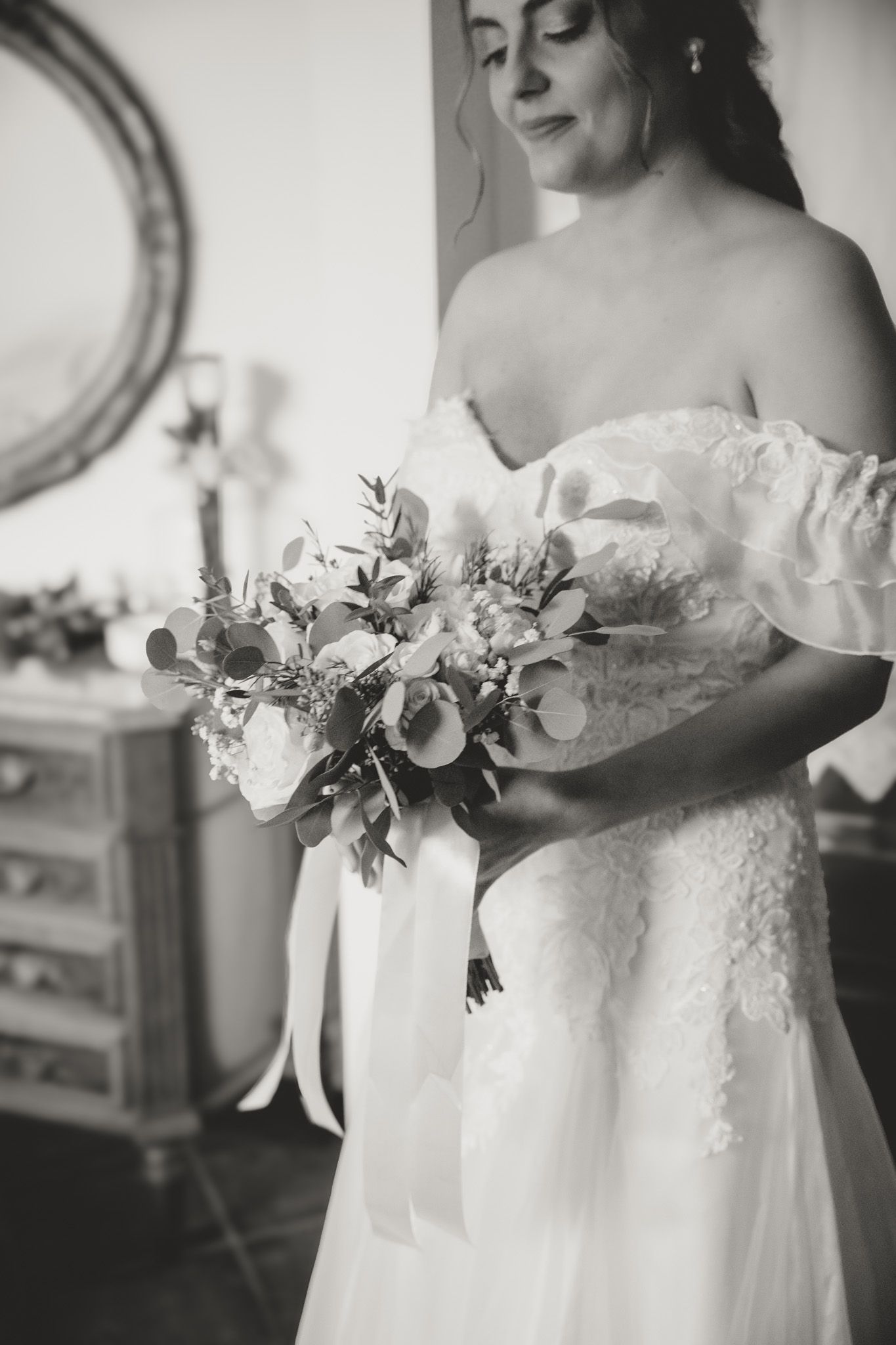 Black and white photo showing delicate lace details and floral bouquet on a wedding dress.