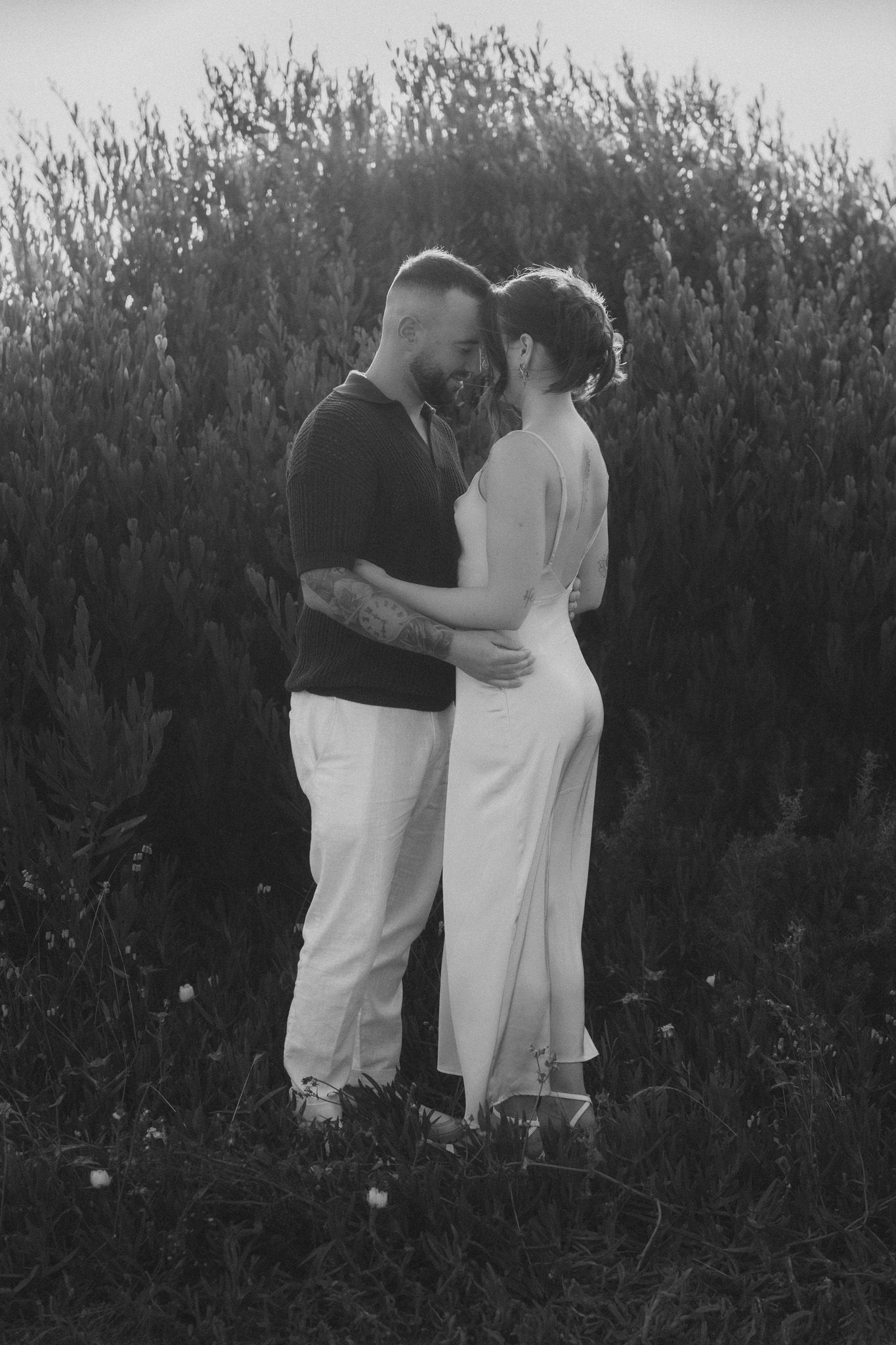 Black and white photo of two people sharing a tender moment among tall grass.