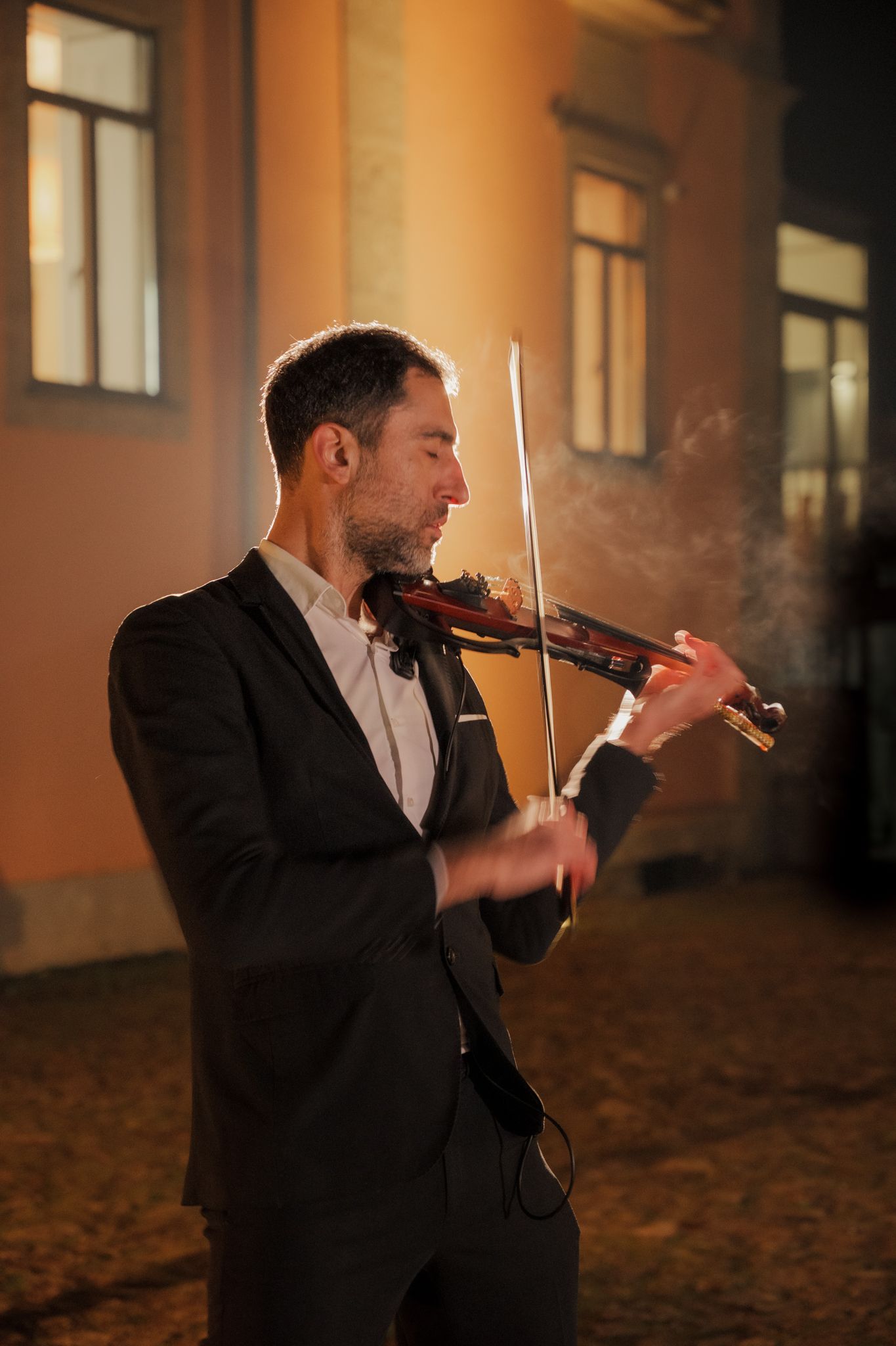 Musician plays violin in formal attire under warm lighting.