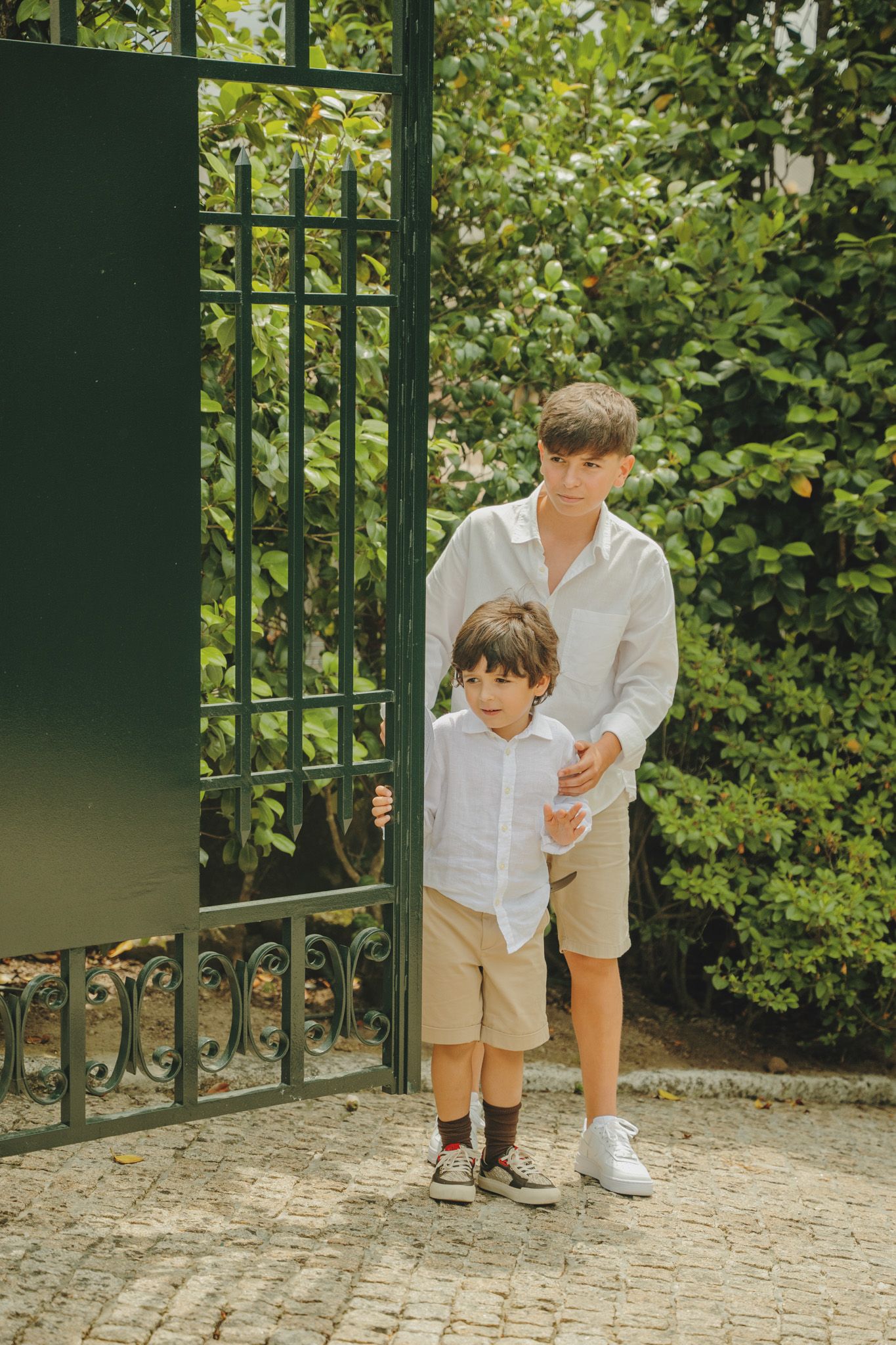Adult and child in matching white shirts and khaki shorts by garden gate.