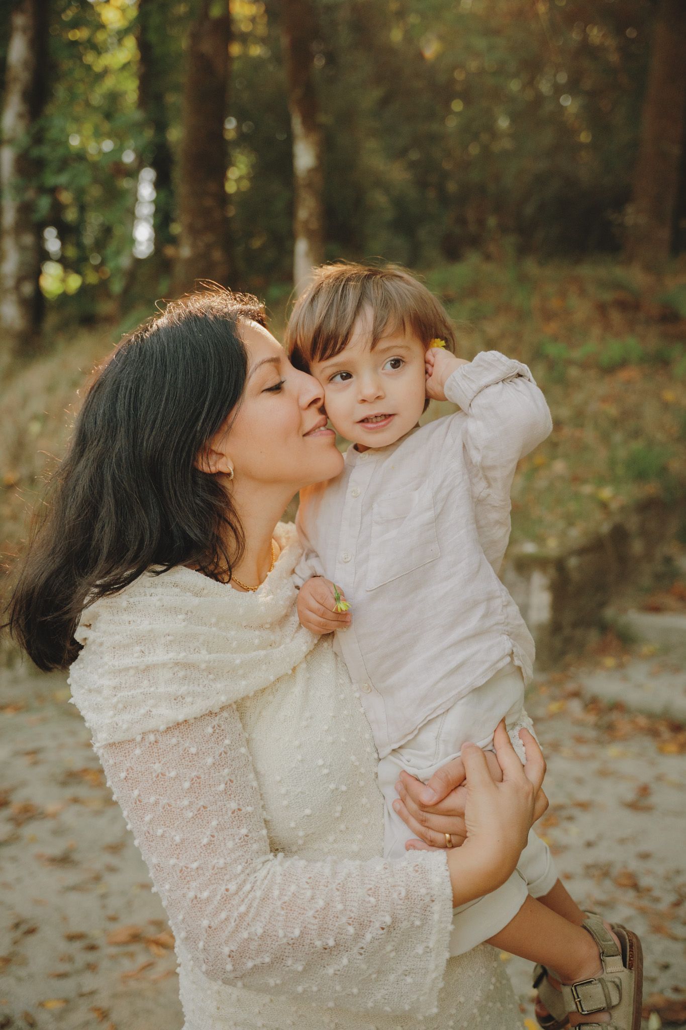 A tender moment between parent and child in white sweaters against an autumn forest backdrop.