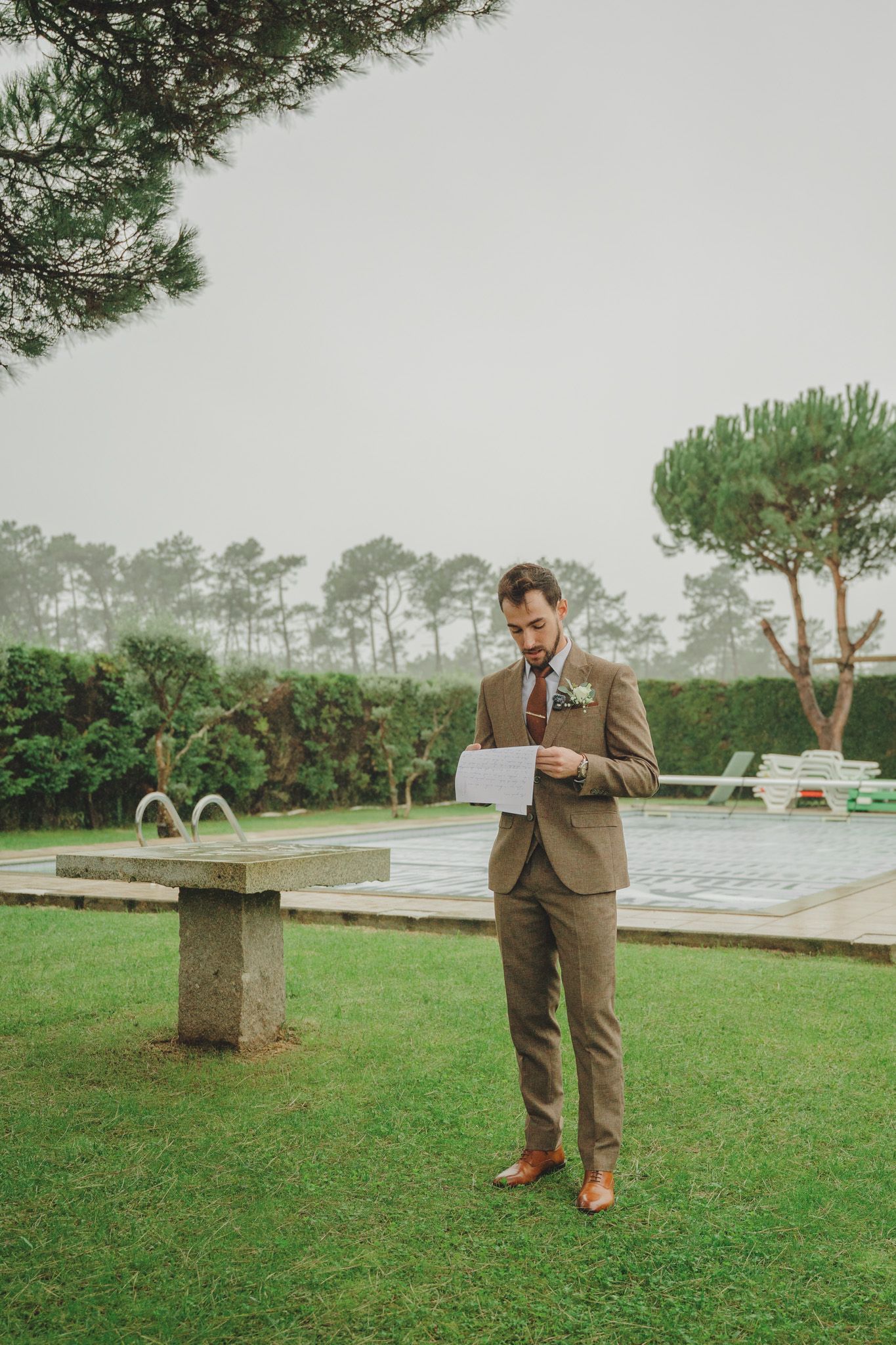 Person in brown suit walking on grass with pine trees in background.