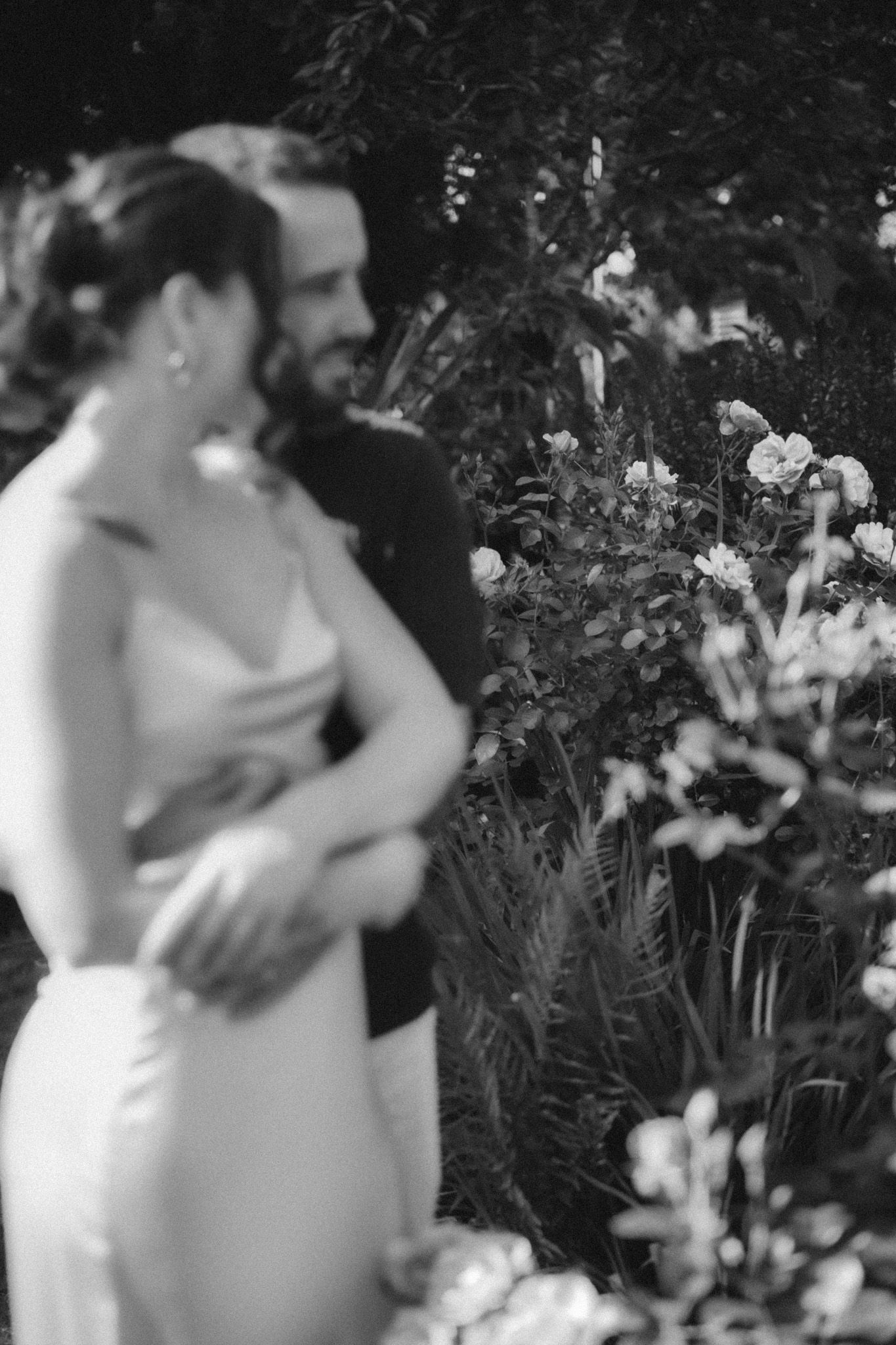 Soft focus black and white portrait of couple among blooming garden flowers.