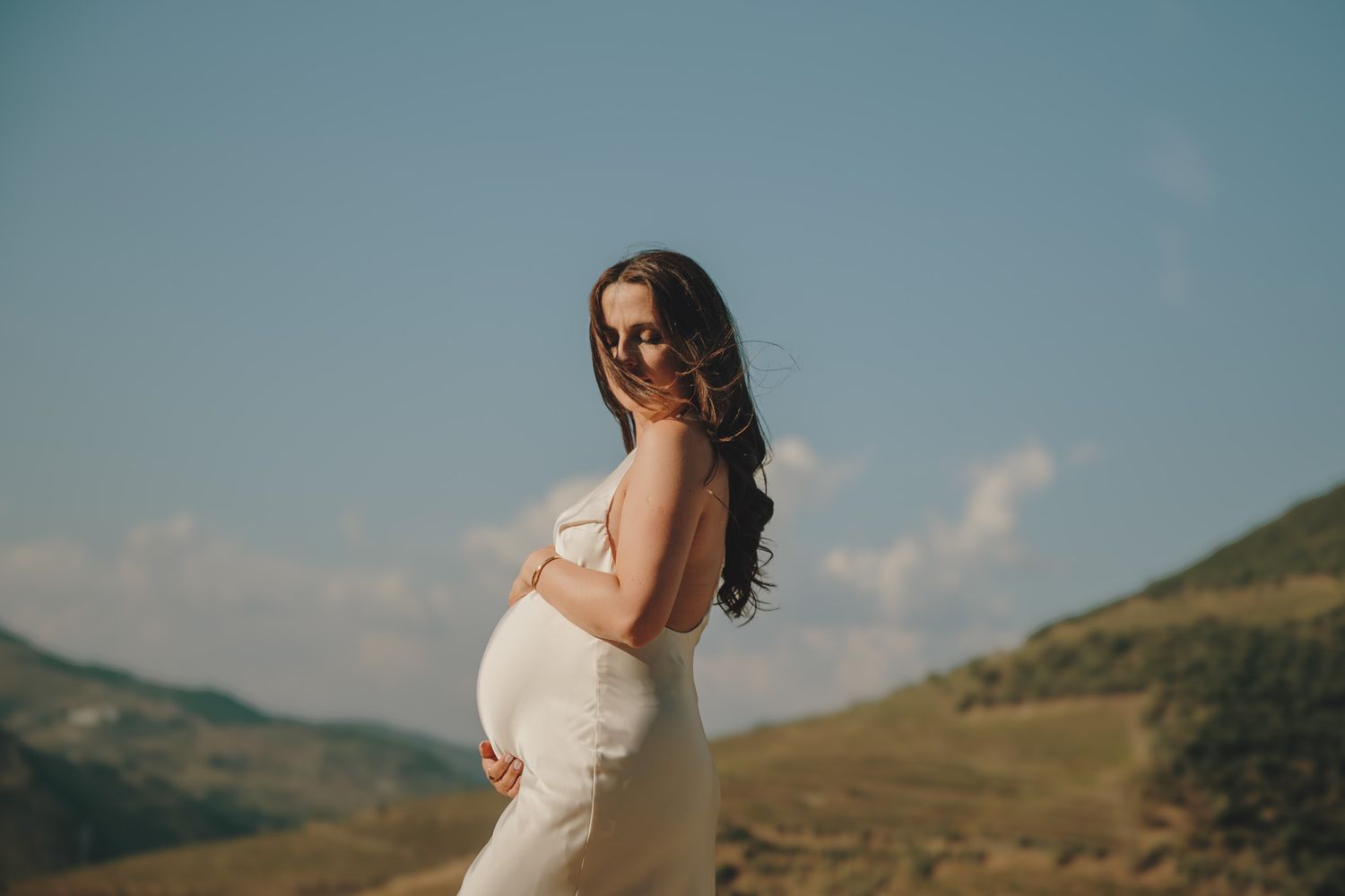 A flowing white dress catches the breeze against a backdrop of sun-drenched mountains and valleys.