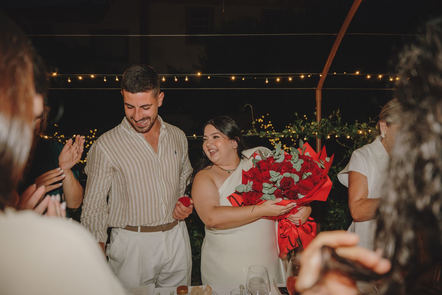 Evening celebration with guests seated at decorated tables under string lights.