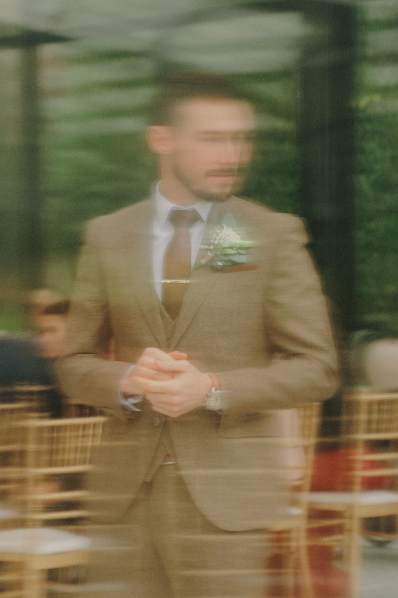 Motion-blurred image of suited figures in warm brown tones at an outdoor event.