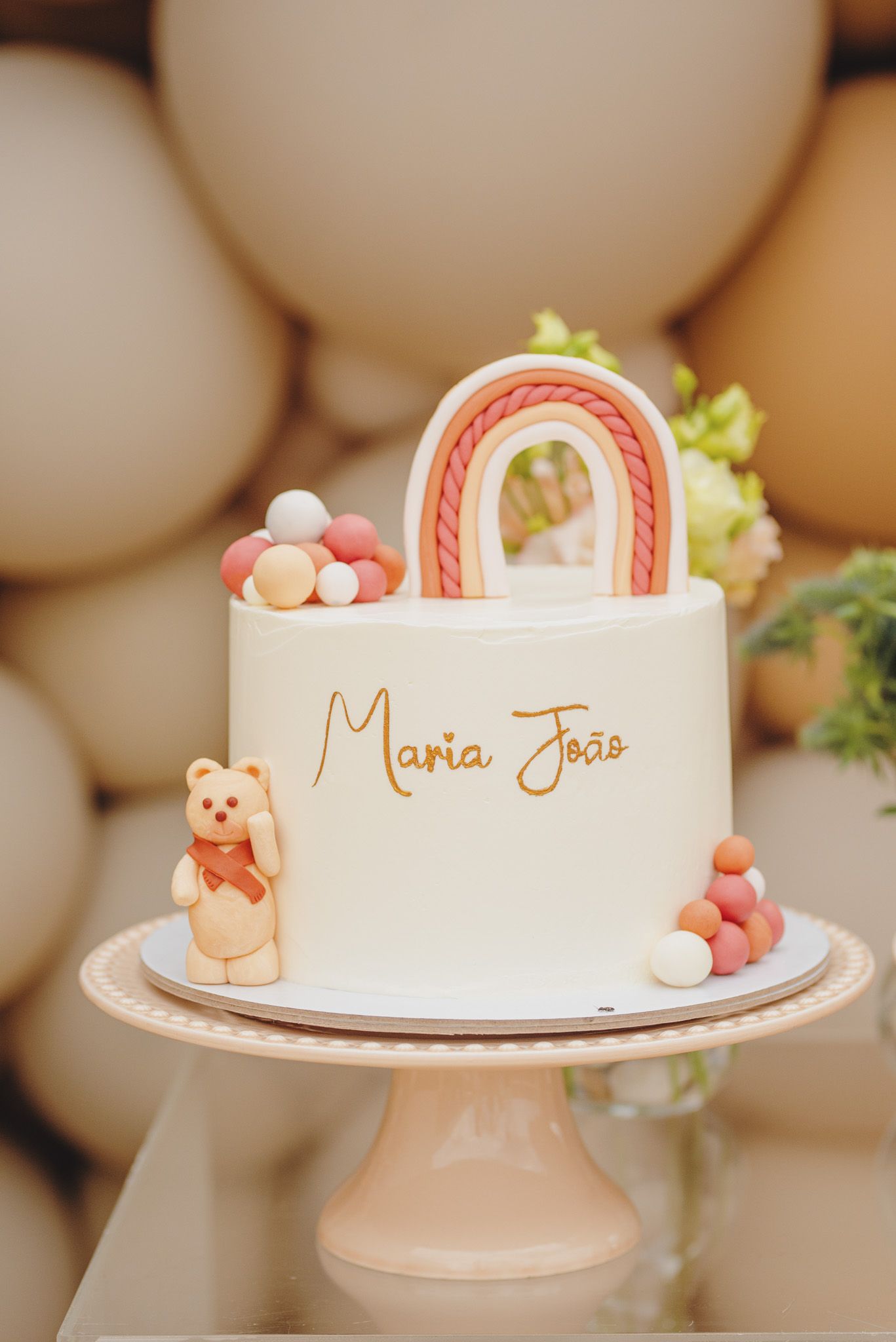 White celebration cake decorated with pink candy arches and gold lettering on a pink cake stand.