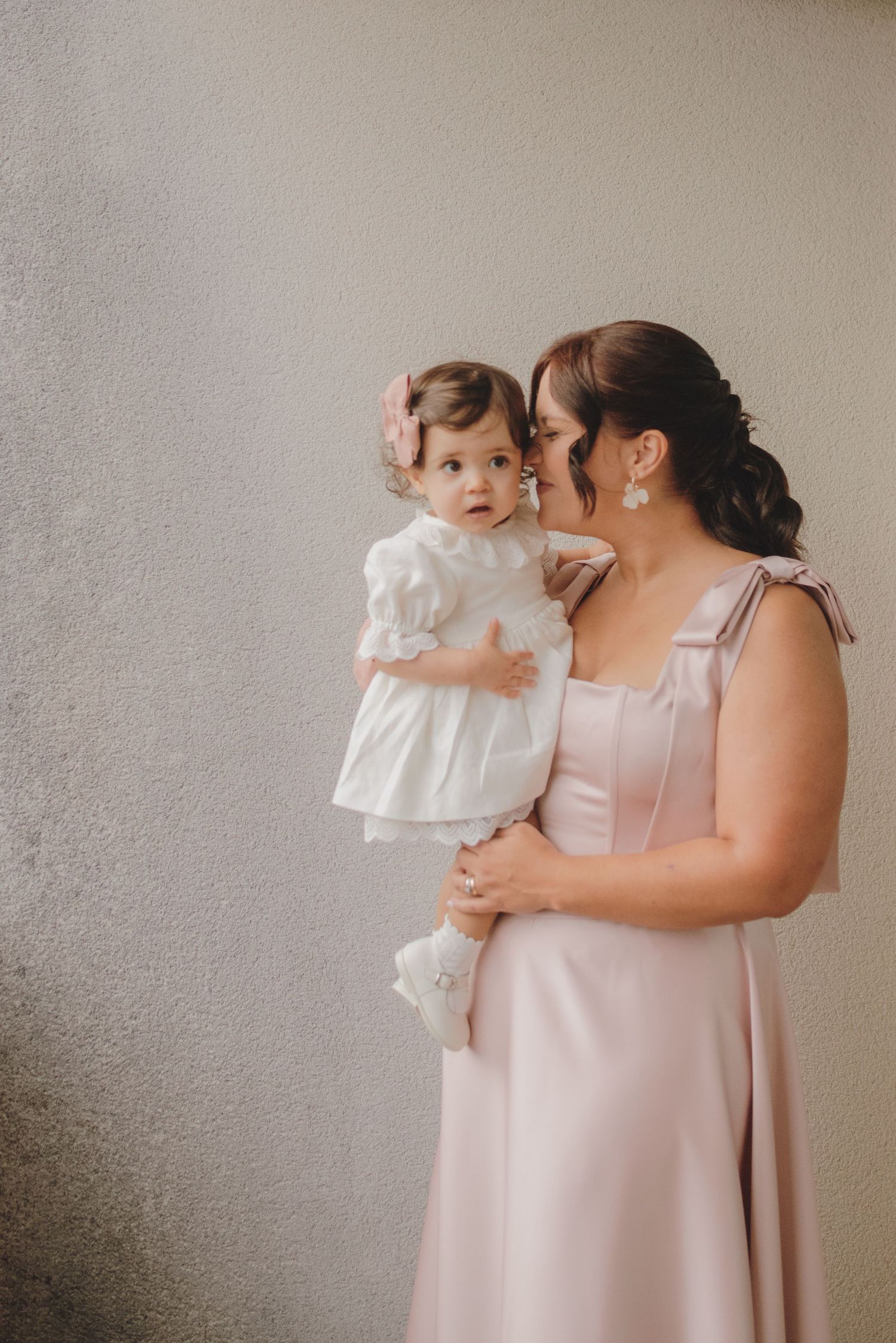 A tender moment captured in soft lighting as a parent in a blush pink dress holds and embraces a small child in white.