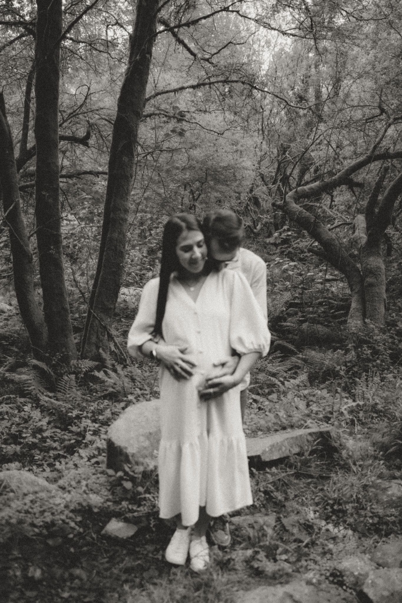Black and white images of a couple sharing intimate moments in a wooded setting.