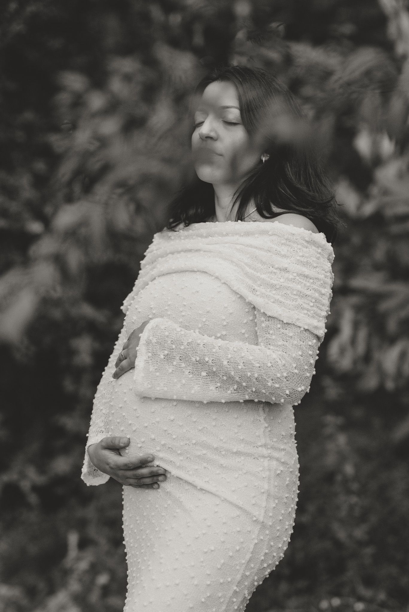 Artistic black and white maternity portrait showing an off-shoulder gown in natural lighting.