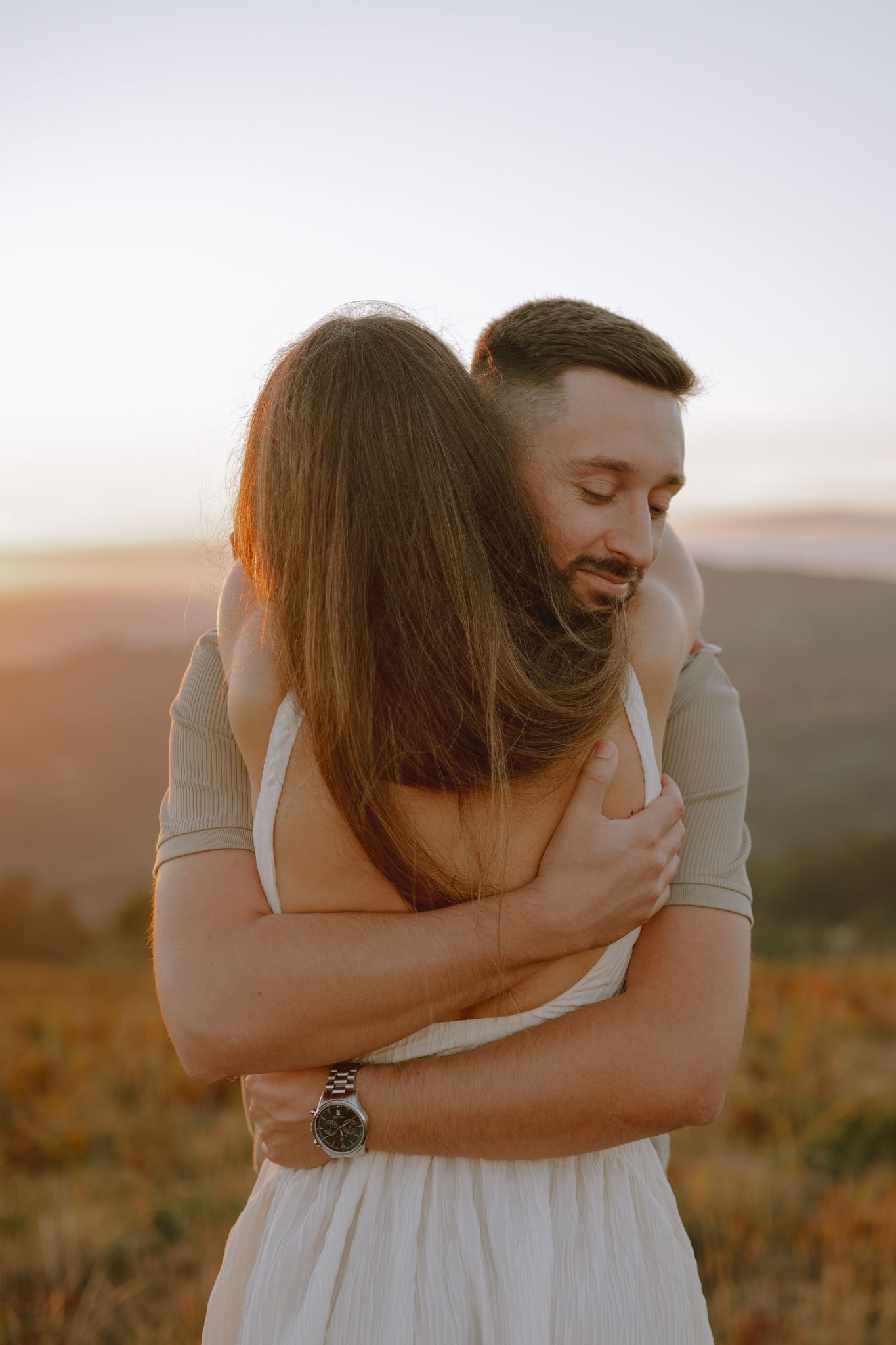 Intimate embrace captured during sunset in a field with warm golden lighting.