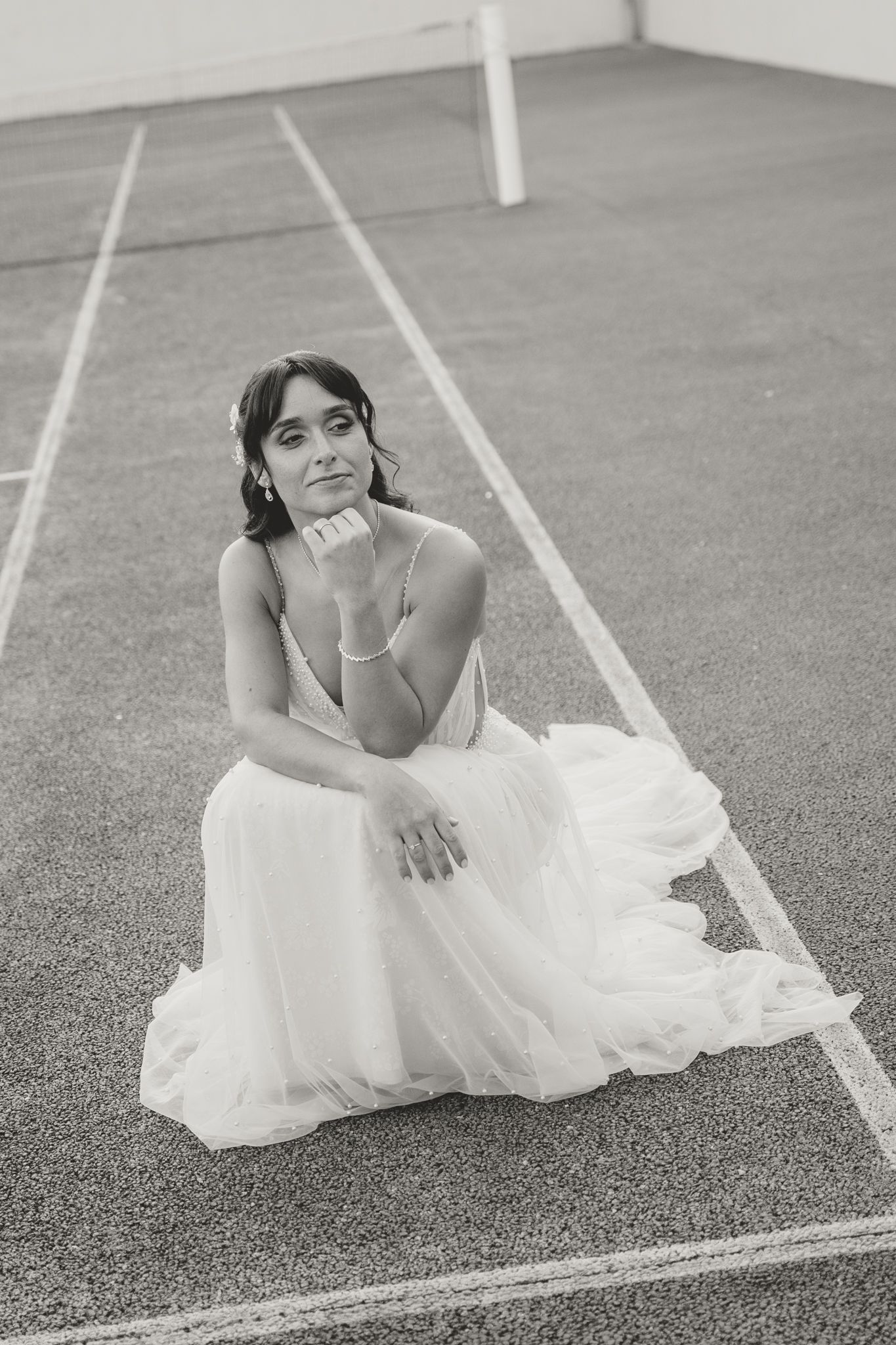 Artistic black and white portrait of bride reclining on sports court with white lines.