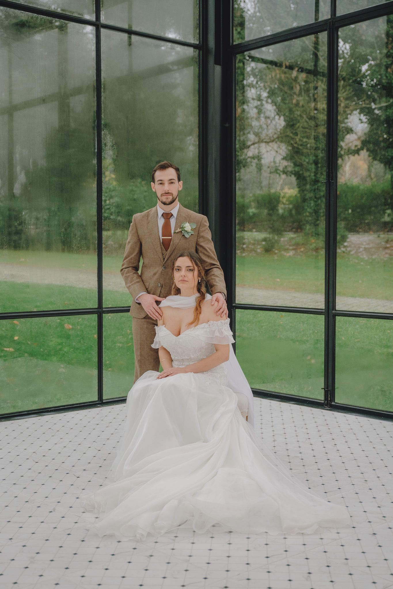 Couple shares intimate moment in modern glass greenhouse with tiled floor and natural lighting.