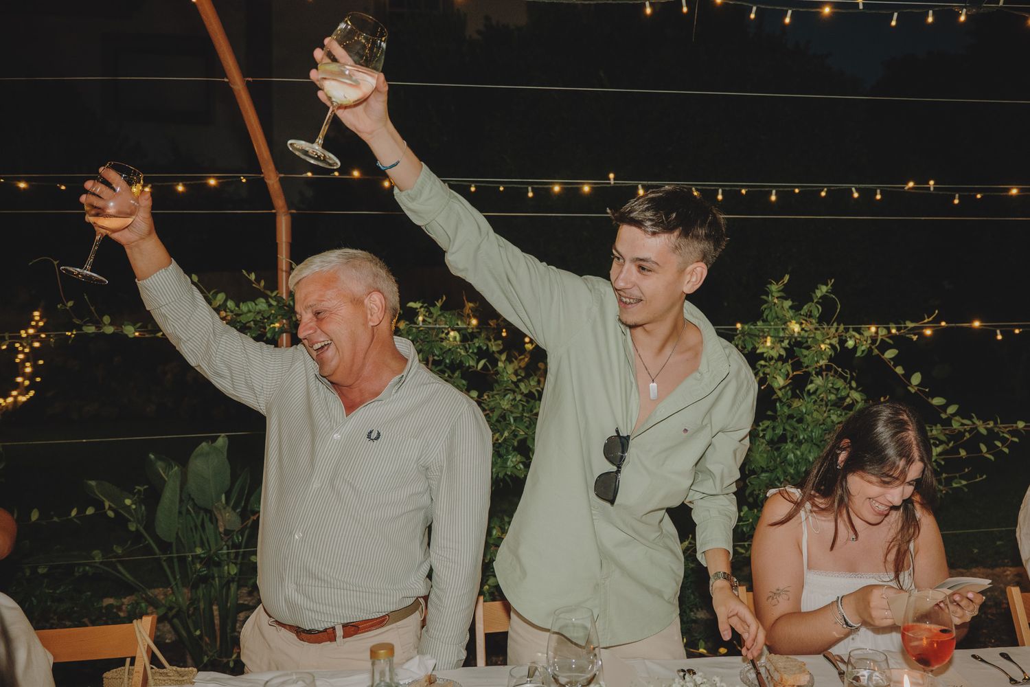 Wedding guests standing and cheering during outdoor reception celebrations.