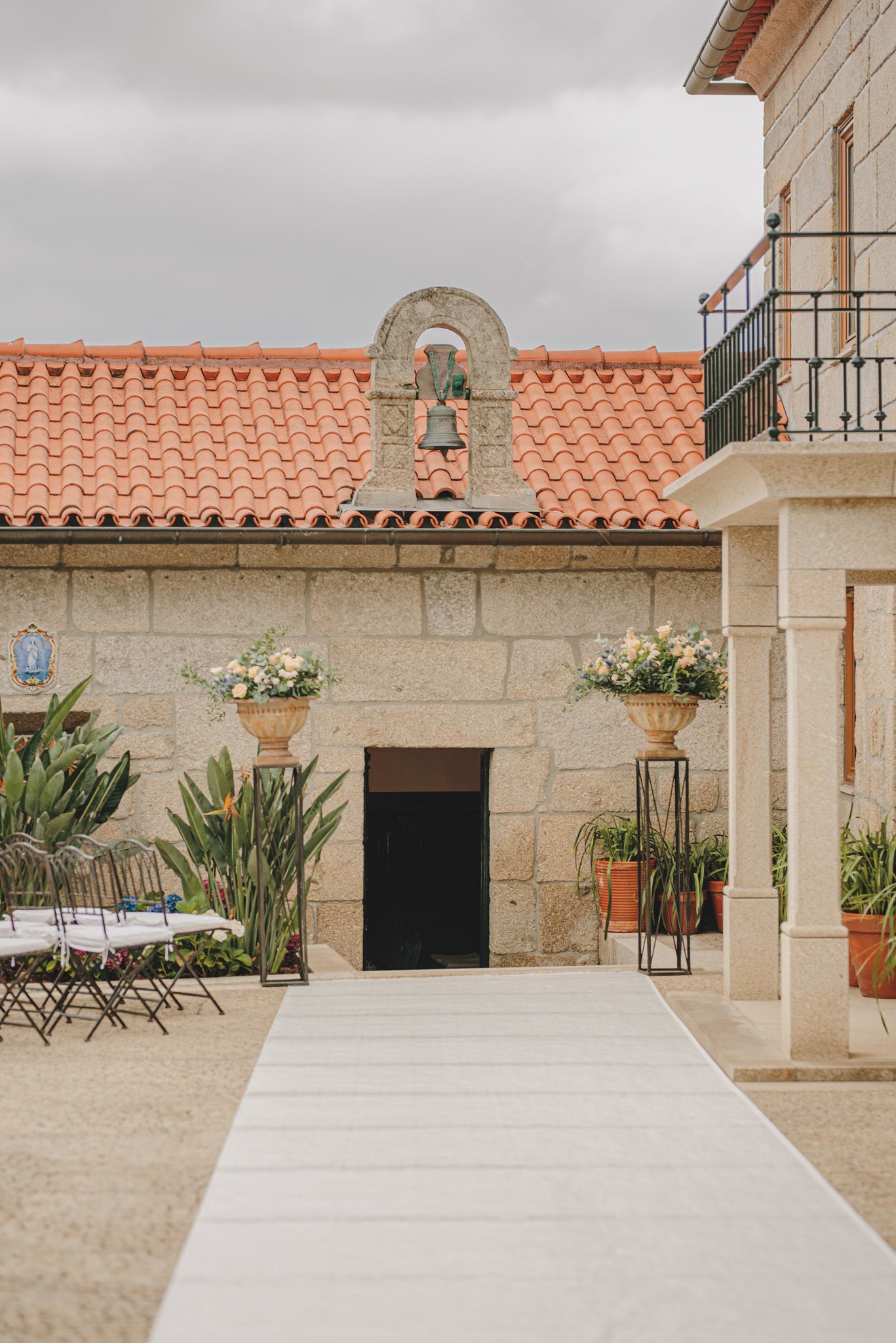 Mediterranean-style courtyard with terracotta roof tiles and stone walls under cloudy skies.
