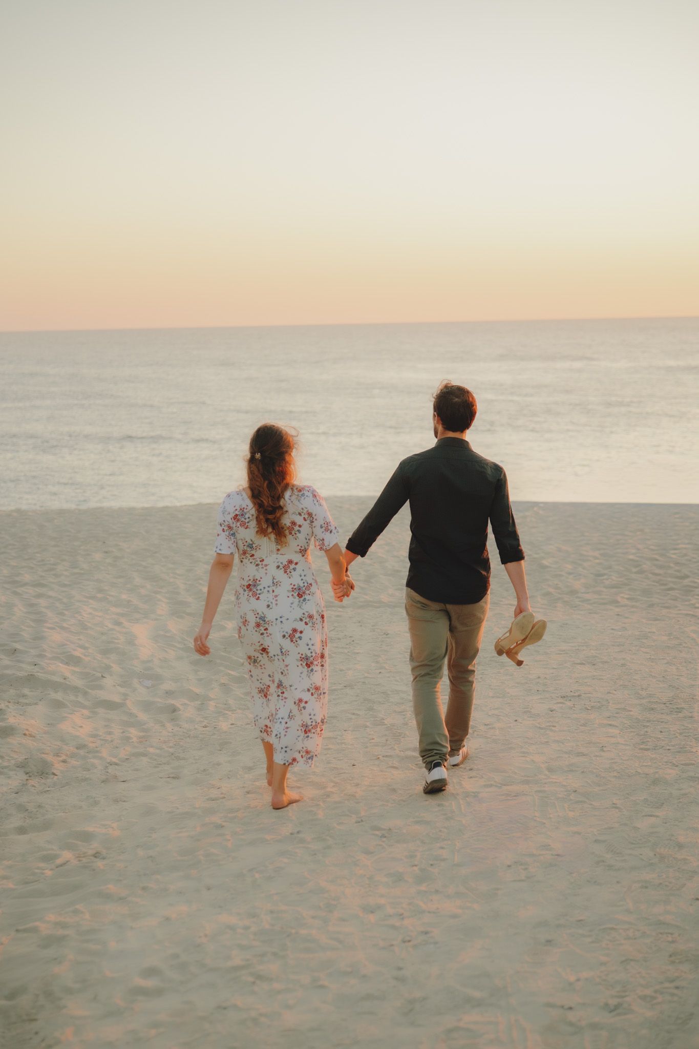 Two people walking together on a sandy beach at sunset with soft golden light.
