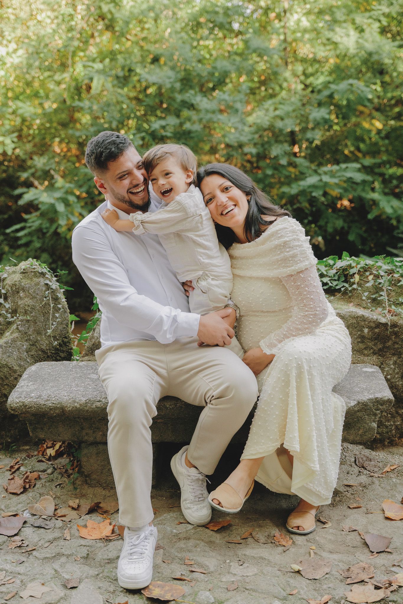 Family dressed in white outfits laughs together during outdoor photo session.