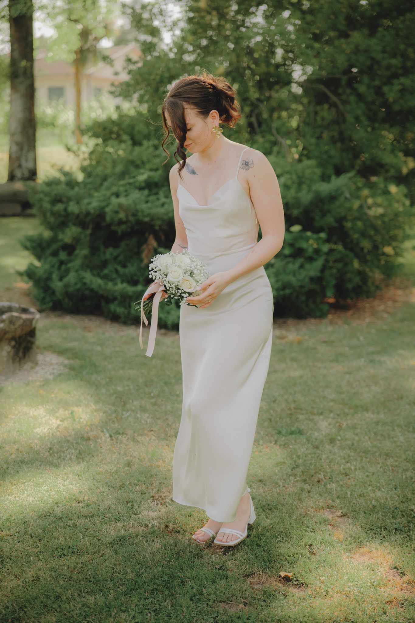 A person in a white dress holds a bouquet while standing in a garden setting.