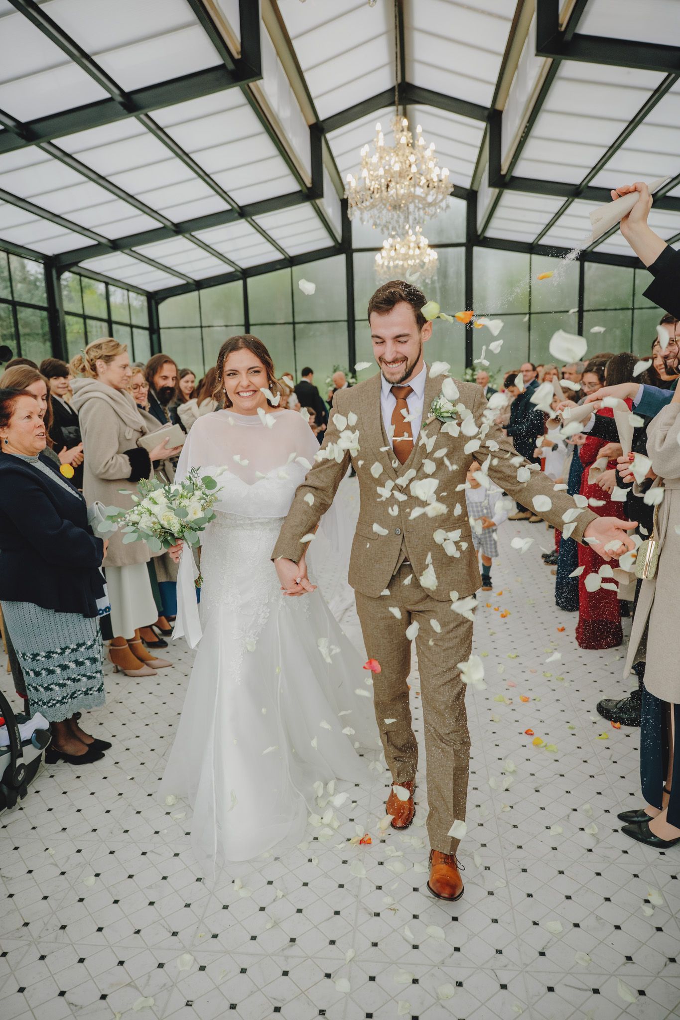 Wedding celebration in glass conservatory with confetti shower and chandelier overhead.