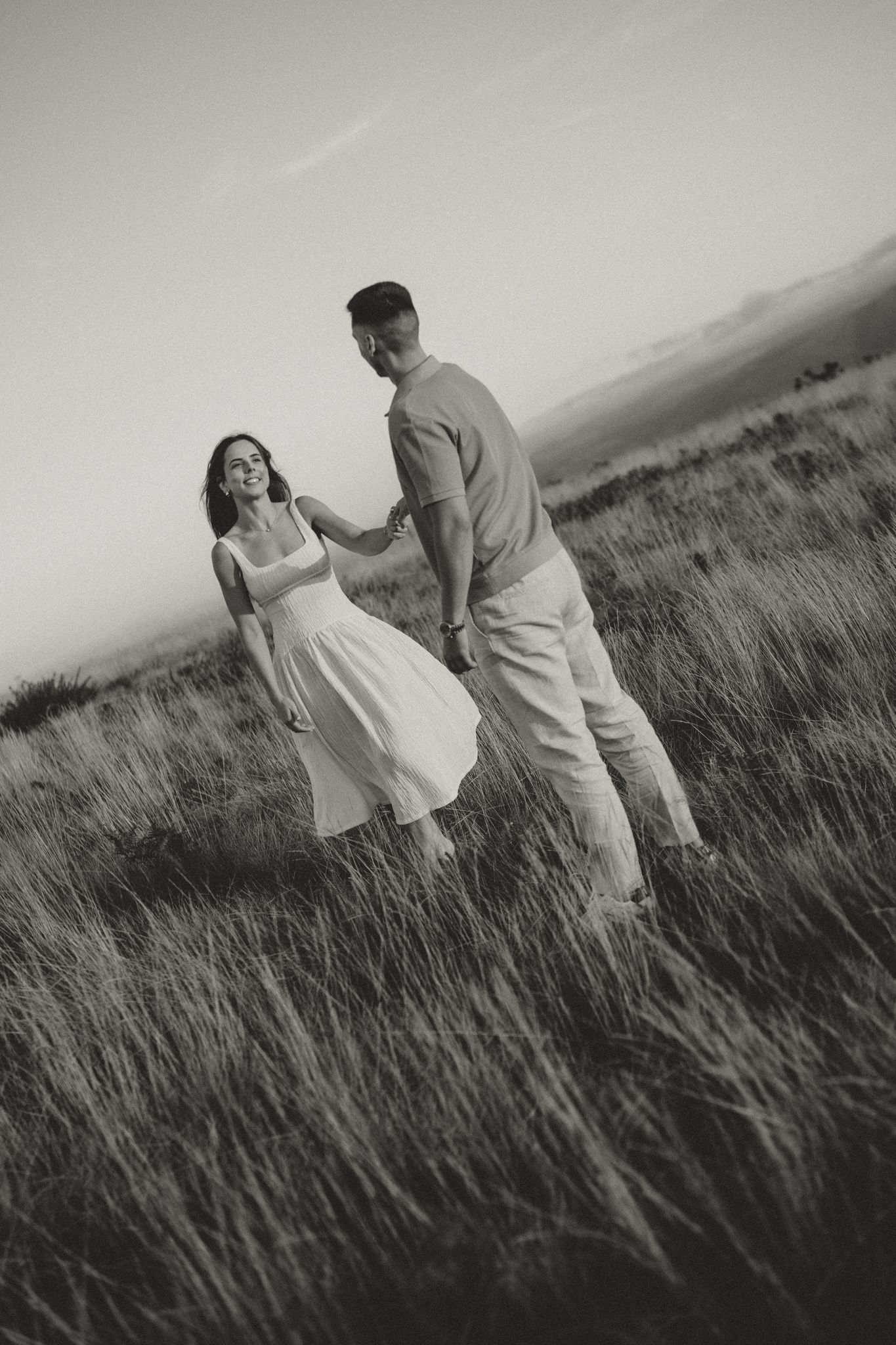 A couple shares tender moments in a monochrome photo shoot in a grassy field.