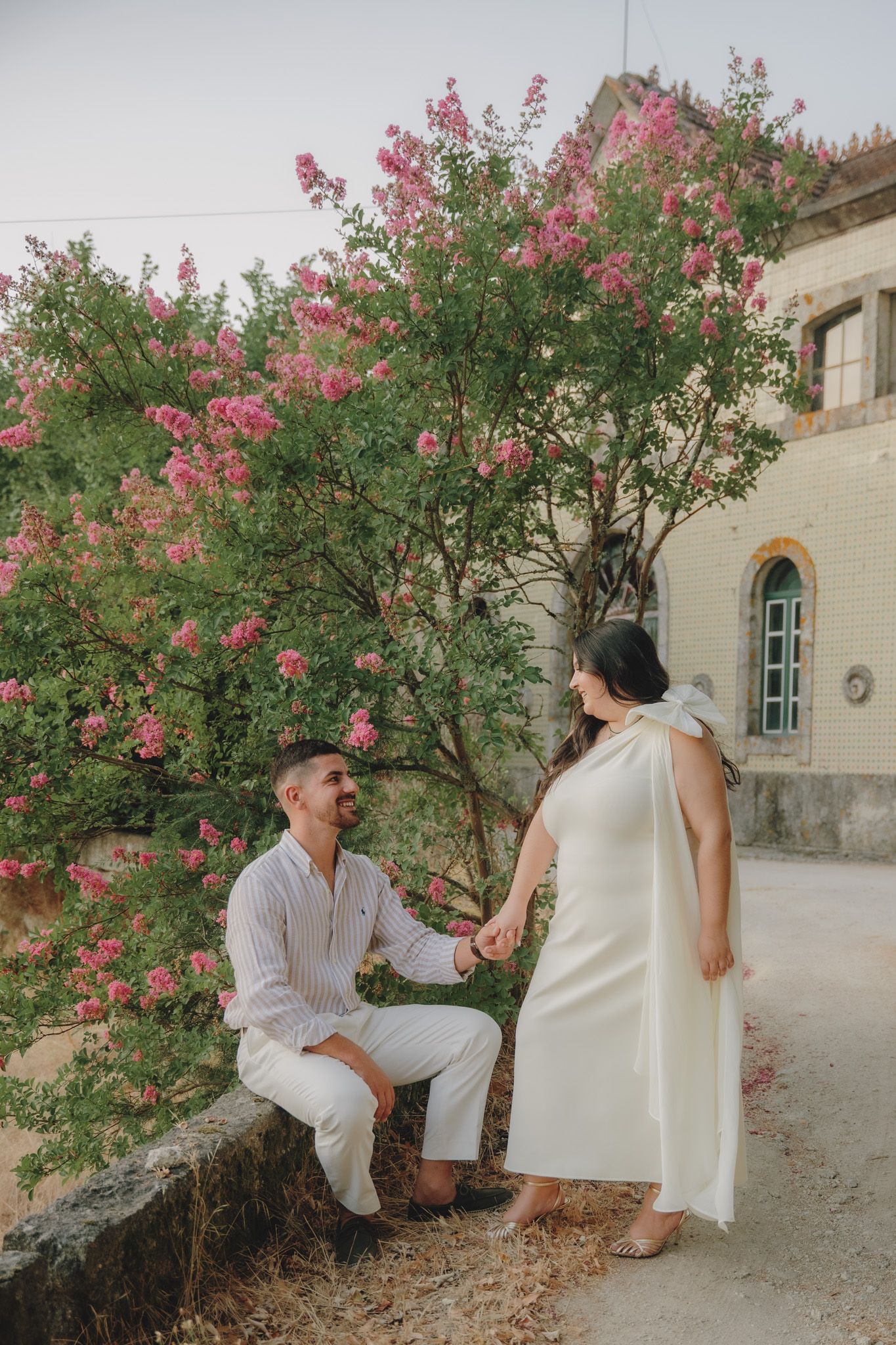 A romantic sequence of poses between two people in white clothing near blooming pink flowers and stone walls.
