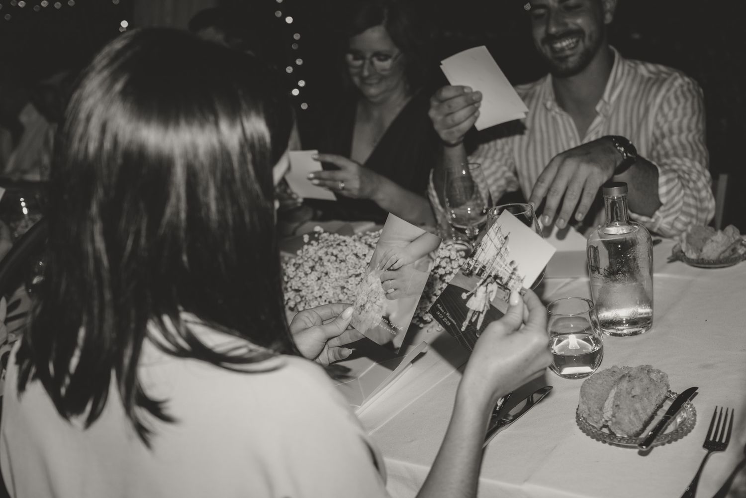Black and white photo of guests sharing food and drinks at a festive dinner table.